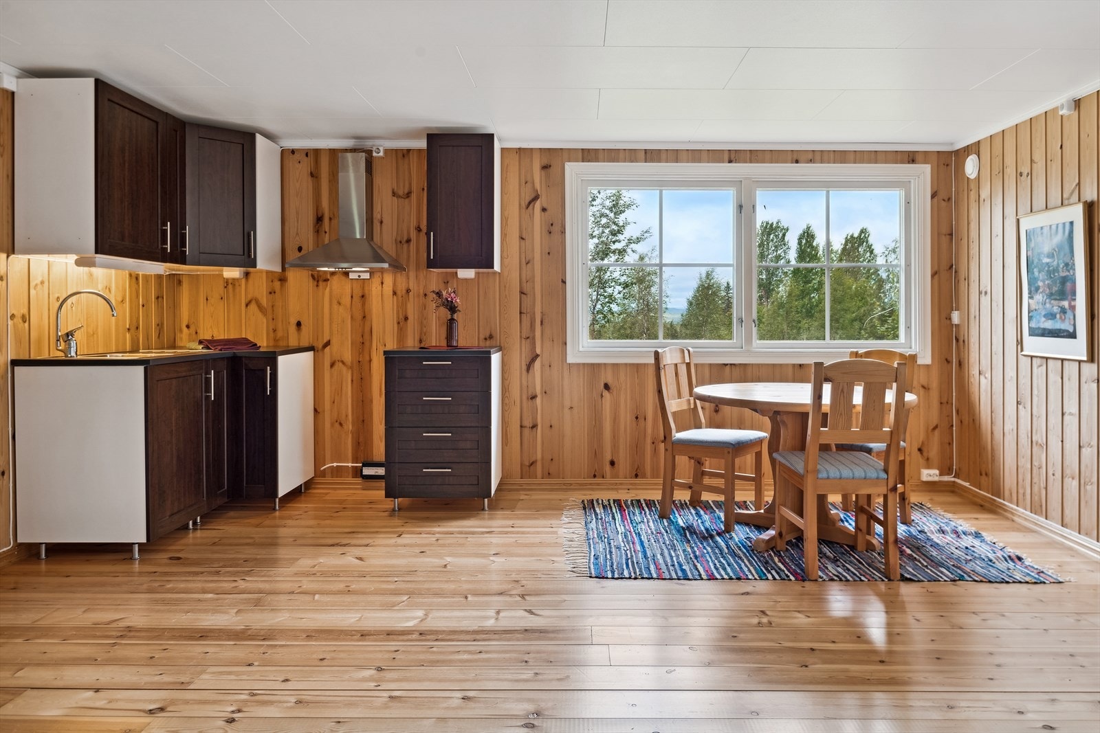 Kjøkkeninnredning med mørklaminerte profilerte fronter, laminerte skrog og benkeplater. Innredningen består av seks skap og en skuffeseksjon. Avsatt plass til komfyr under vifta og til kjøleskap. Galleribilde