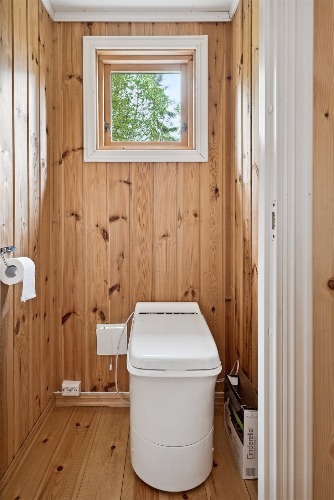 Toalettrom med stående panel på veggene og overflatebehandlet furu. Rommet er innredet med Cinderella forbrenningstoalett. Galleribilde