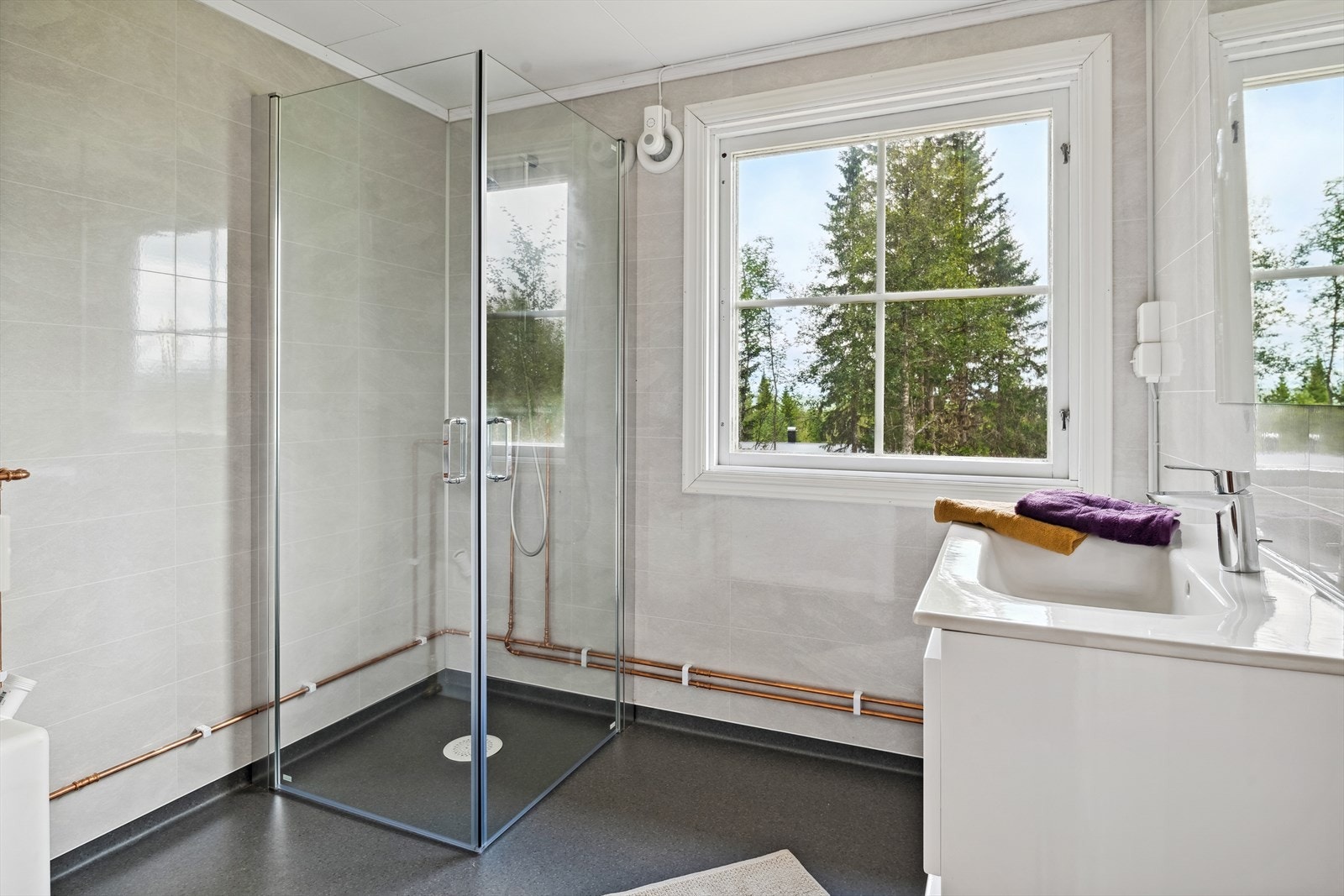 Innredning med heldekkende servant i hvit skuffeinnredning, speil med lys over, dusjhjørne med dører og dusjarmatur montert på vegg og varmtvannsbereder. Galleribilde