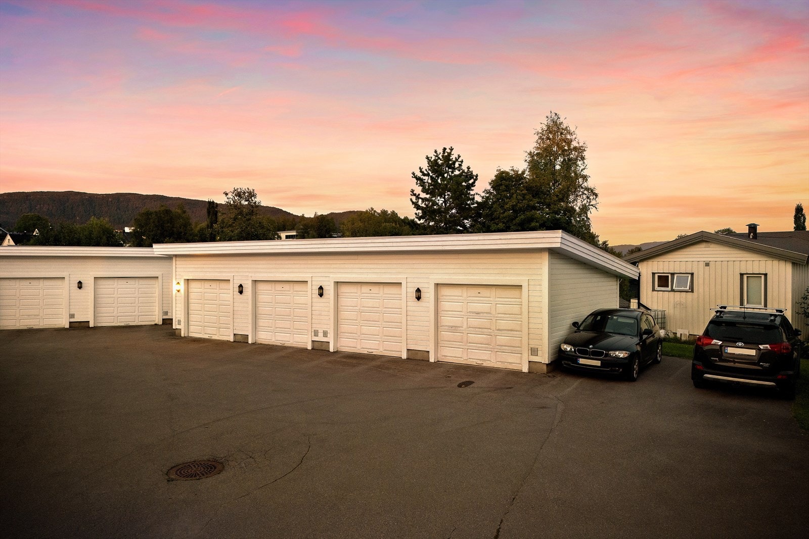 Her ser man bilde fra felles gårdtun som er asfaltert. Borettslaget har velstelte utenomhusarealer med gressplener. Elbillader montert i garasjen. Galleribilde