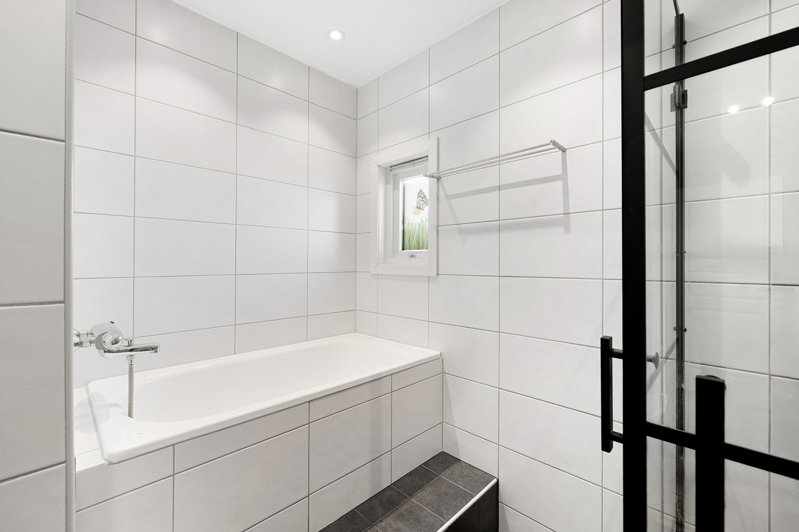 Rommet er innredet med både dusjhjørne med stilrene svarte sprosser og et praktisk badekar. Galleribilde