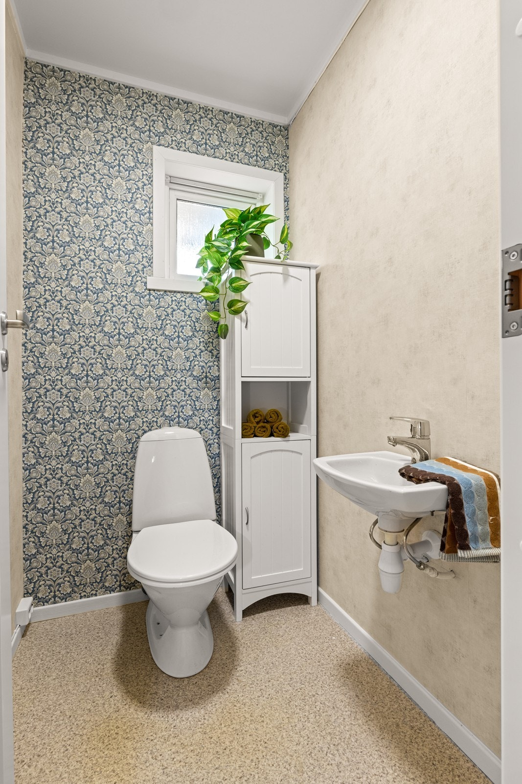 Toalettrommet har praktisk utforming med belegg på gulv og tapet på vegger, som gir et enkelt og funksjonelt uttrykk. Rommet er utstyrt med toalett og servant. Galleribilde