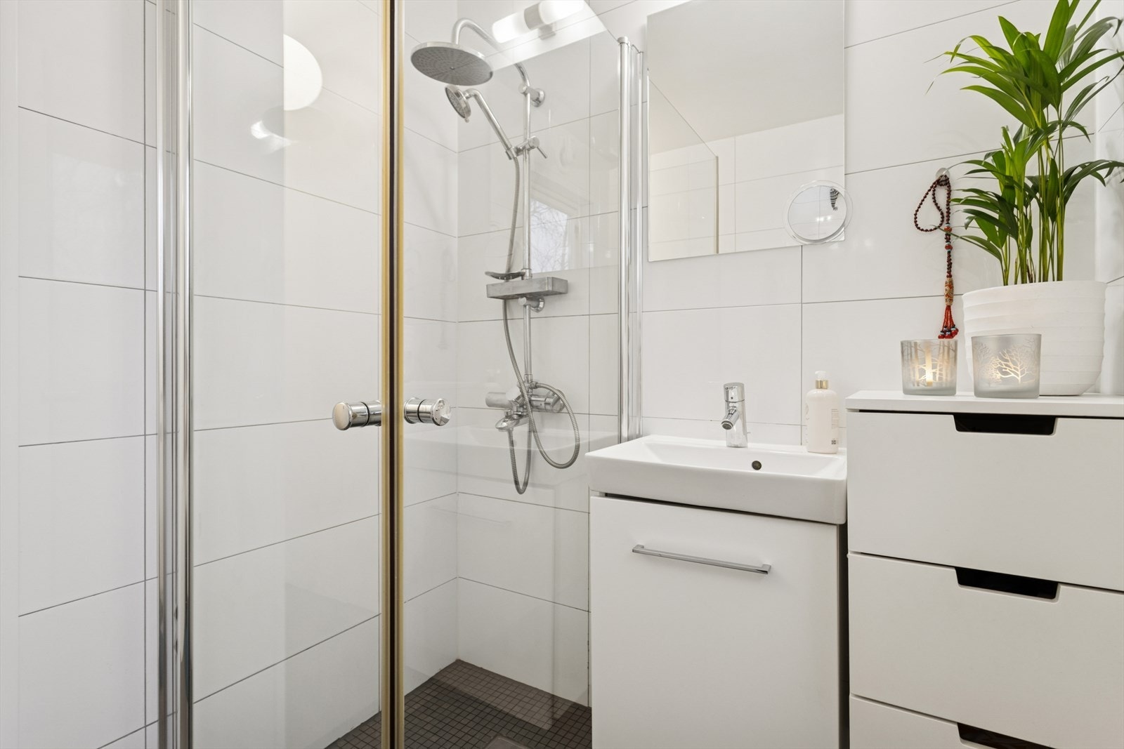 Badet er utstyrt med dusjvegger av glass, dusjgarnityr på vegg og innredning med servant. Det er også opplegg til en mindre vaskemaskin på dette badet. Galleribilde