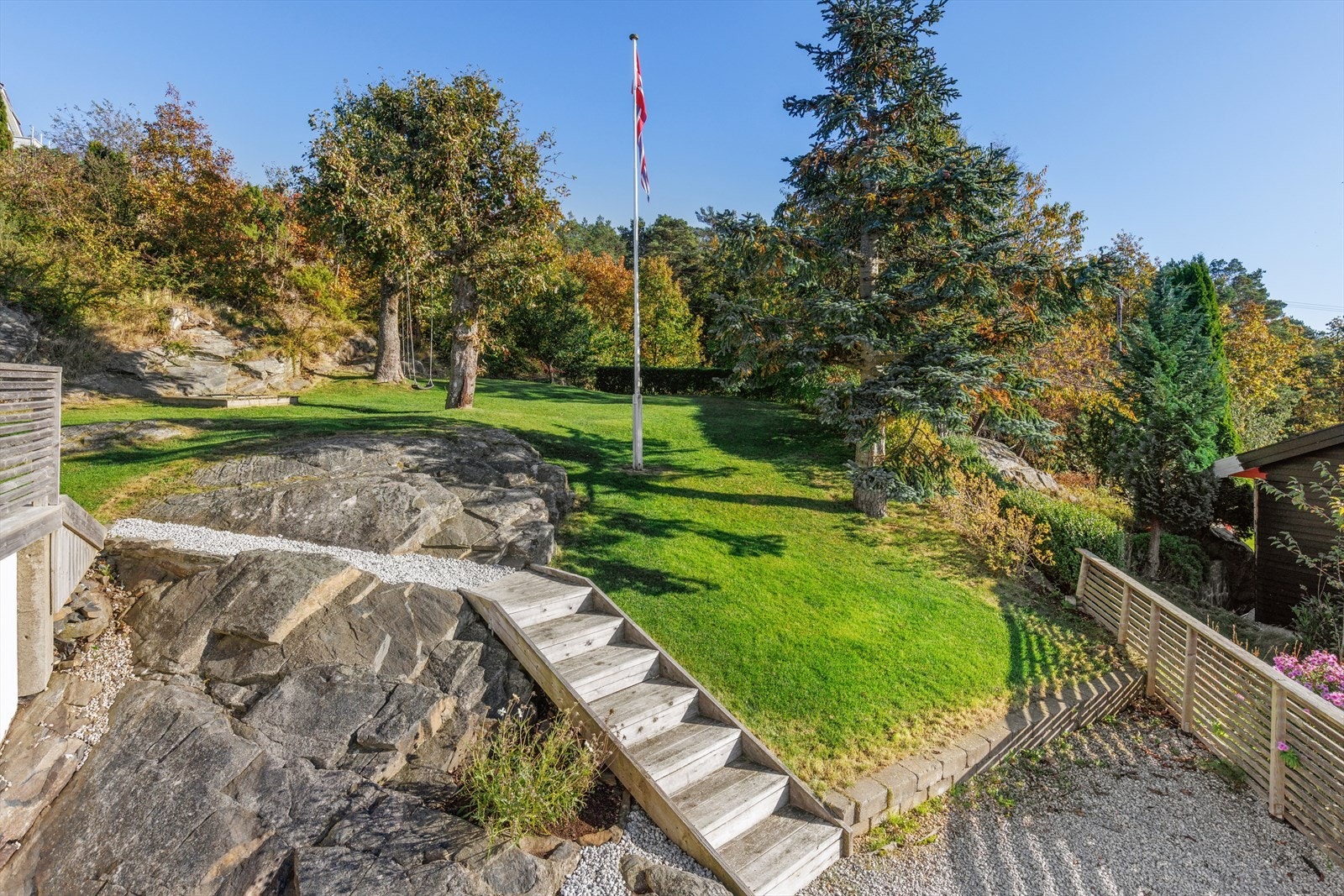 Tomten byr på en nydelig kombinasjon av natur og struktur, med frodig plen, vakre trær og en flaggstang som gir et klassisk preg. Galleribilde