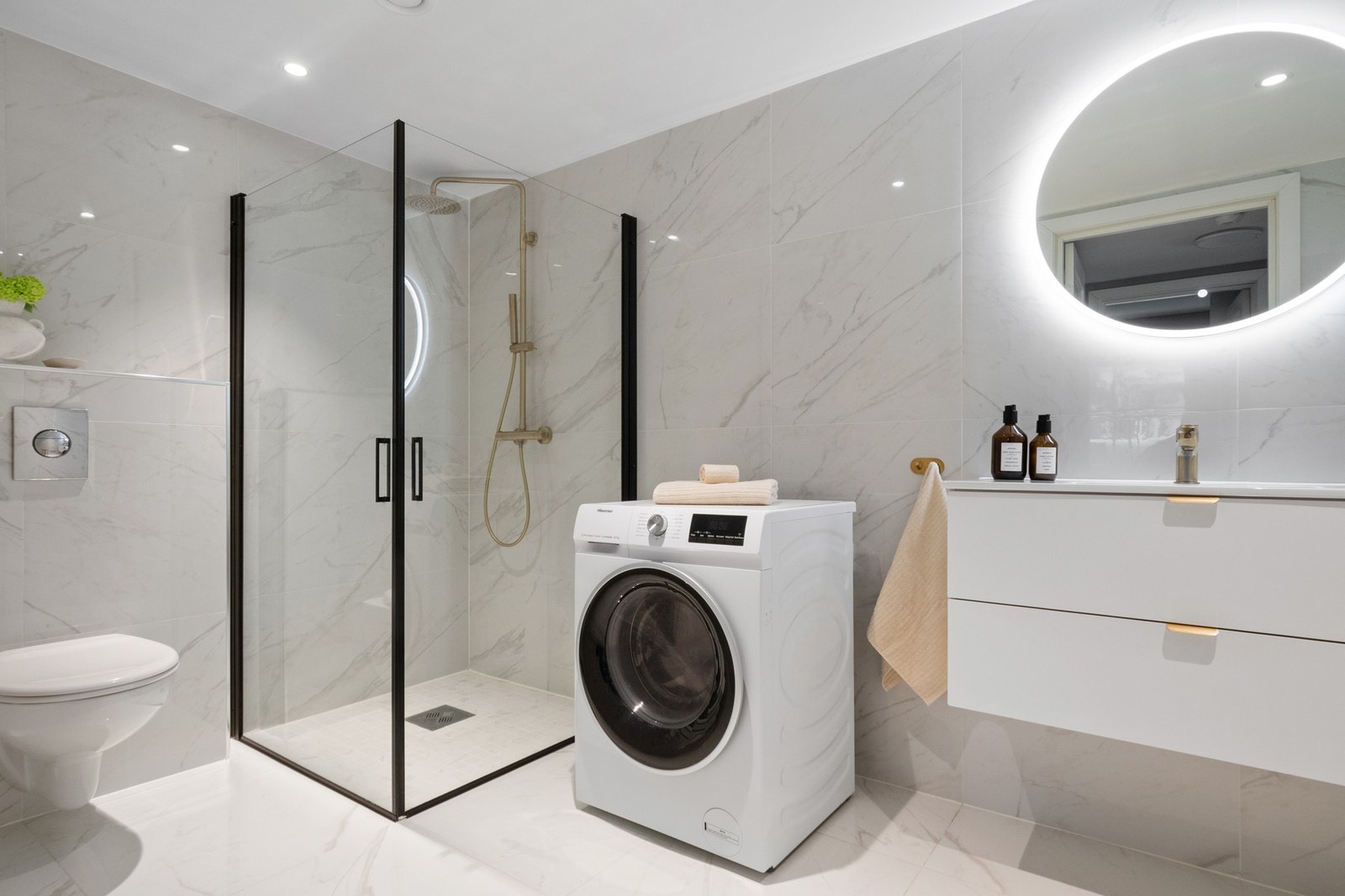 Badet har vegghengt toalett og et dusjhjørne med regnfallsdusj i gullutførelse og innfellbare glassdører. Rommet har opplegg for vaskemaskin. Galleribilde