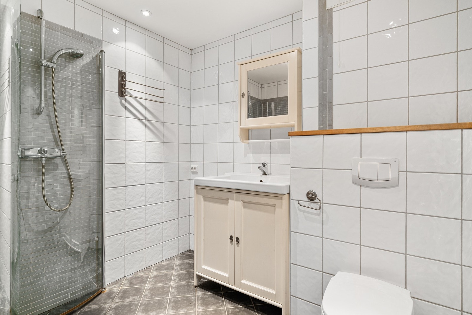 Flislagt bad med innfellbare glassdører, servant, skap med speil og toalett. Galleribilde