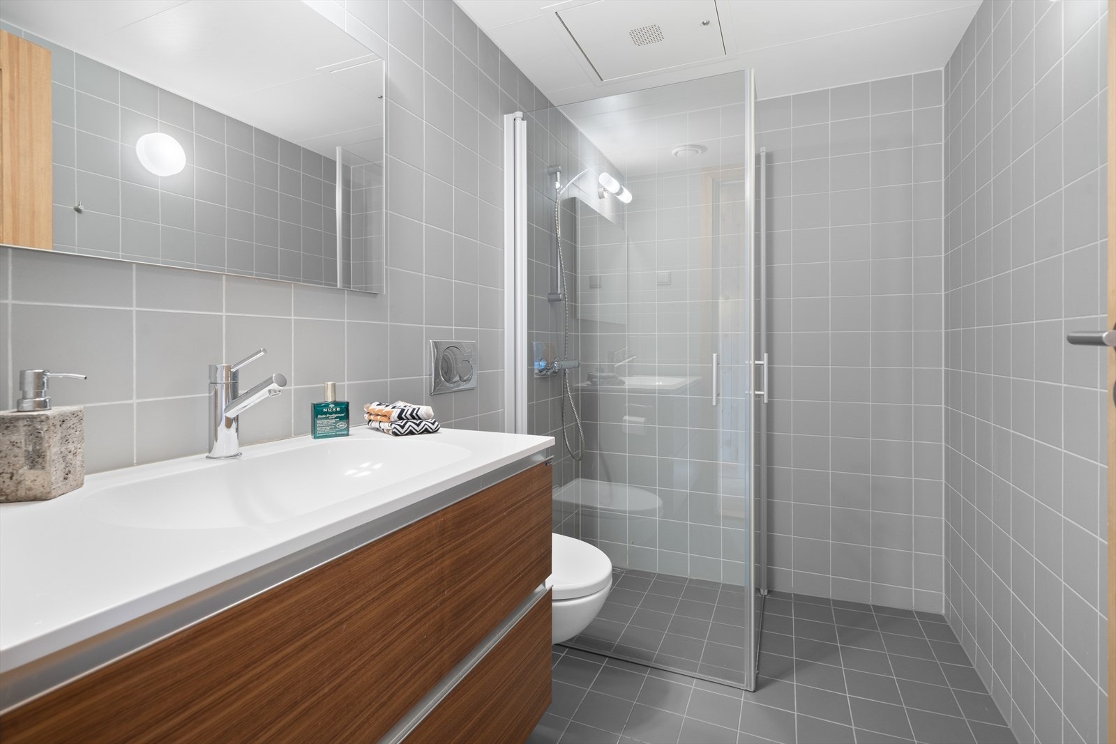 Baderommet i and plan er også både gulv og vegger flislagt. Innredningen med heldekkende servant med ettgreps blandebatteri, et dusjhjørne med glassdører og et blandebatteri med temperaturinnstilling. Galleribilde