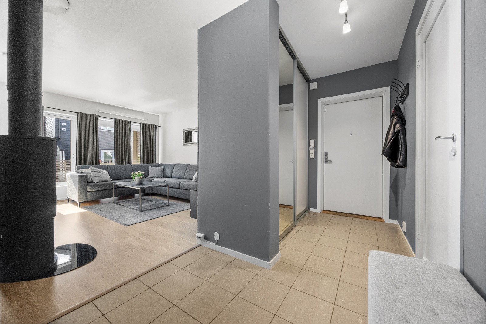 Tiltalende entre med delikate storformatfliser på gulv med underliggende gulvvarme og lysmalte veggflater som gir et godt førsteinntrykk av leiligheten. Det er bygget inn en stilren skyvedørsgarderobe i vegg, perfekt til oppbevaring av ytterklær og sko. Galleribilde