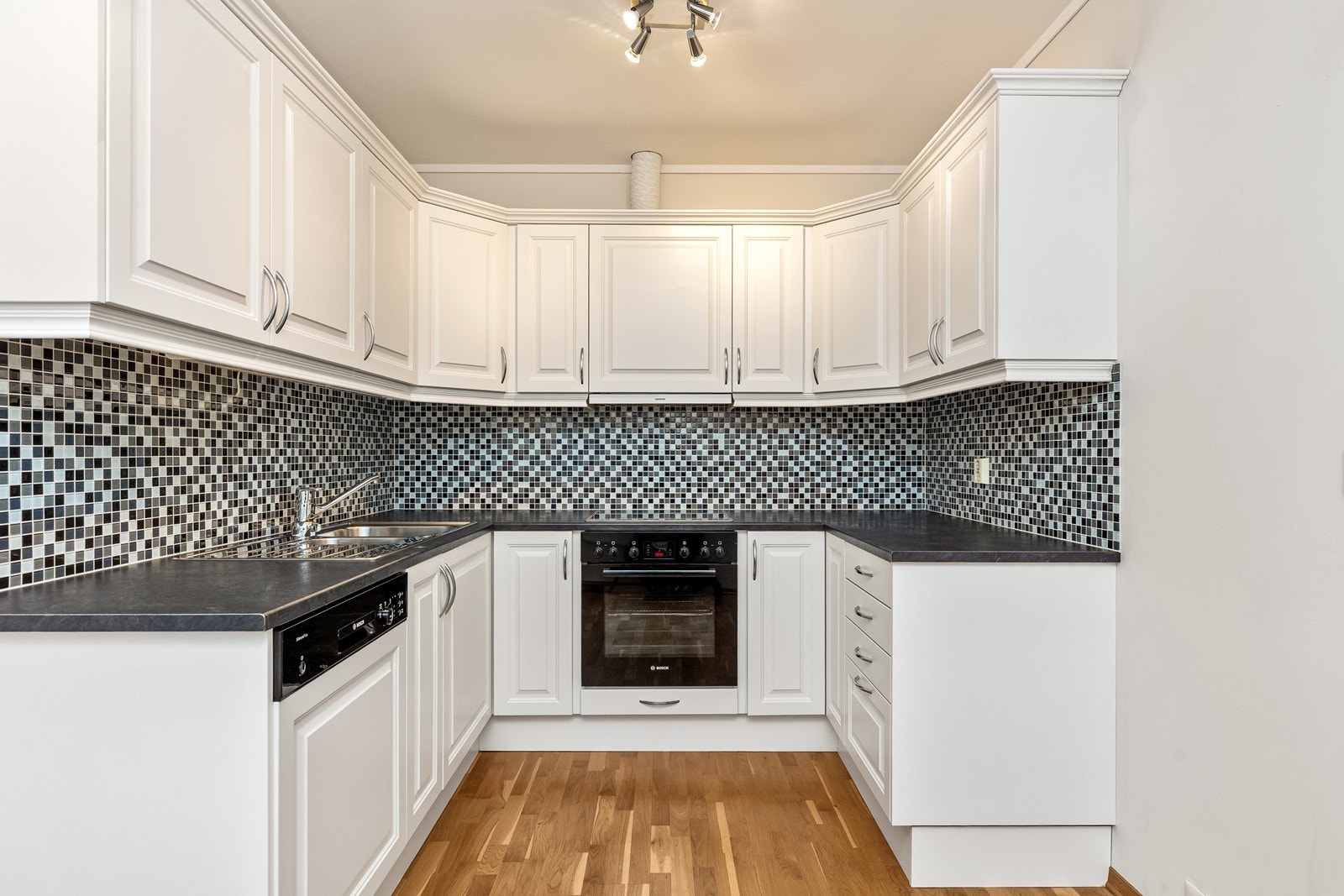 Kjøkkenet er lyst og har en praktisk utforming med godt med skap- og benkeplass. Innredningen har klassiske, hvite profilerte fronter som gir et tidløst uttrykk, og benkeplaten i laminat. Galleribilde