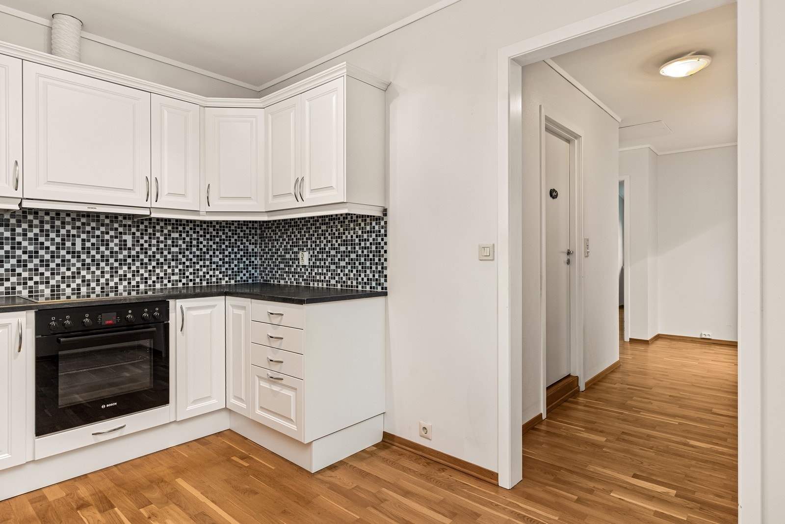 Mellom benkeplate og overskap er det flislagt, noe som gjør det enkelt å holde rent. Av integrerte hvitevarer finner du oppvaskmaskin, komfyr, platetopp og ventilator - en komplett og funksjonell løsning for en effektiv matlaging i hverdagen. Galleribilde