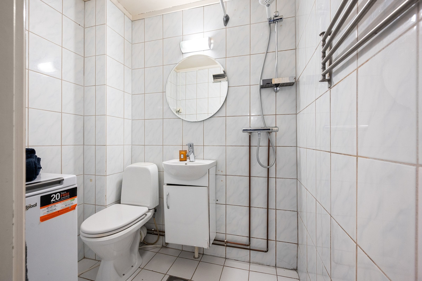 Lyst og flislagt bad. Innredningen består av servant med underskap, speil med lys over, dusjhjørne med forheng og frittstående toalett. Galleribilde