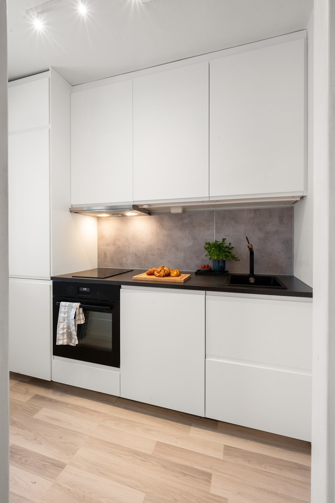 Benkeplate i laminat med fliser på bakvegg, rustfri oppvaskkum og varmtvannsberederen som er også plassert i kjøkkeninnredningen. Galleribilde