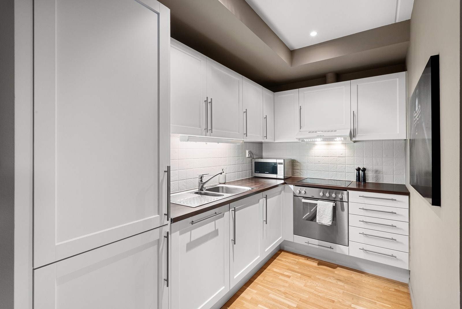 Pent kjøkken med integrerte hvitevarer som platetopp, stekeovn, kjøle/fryseskap og oppvaskmaskin. Galleribilde