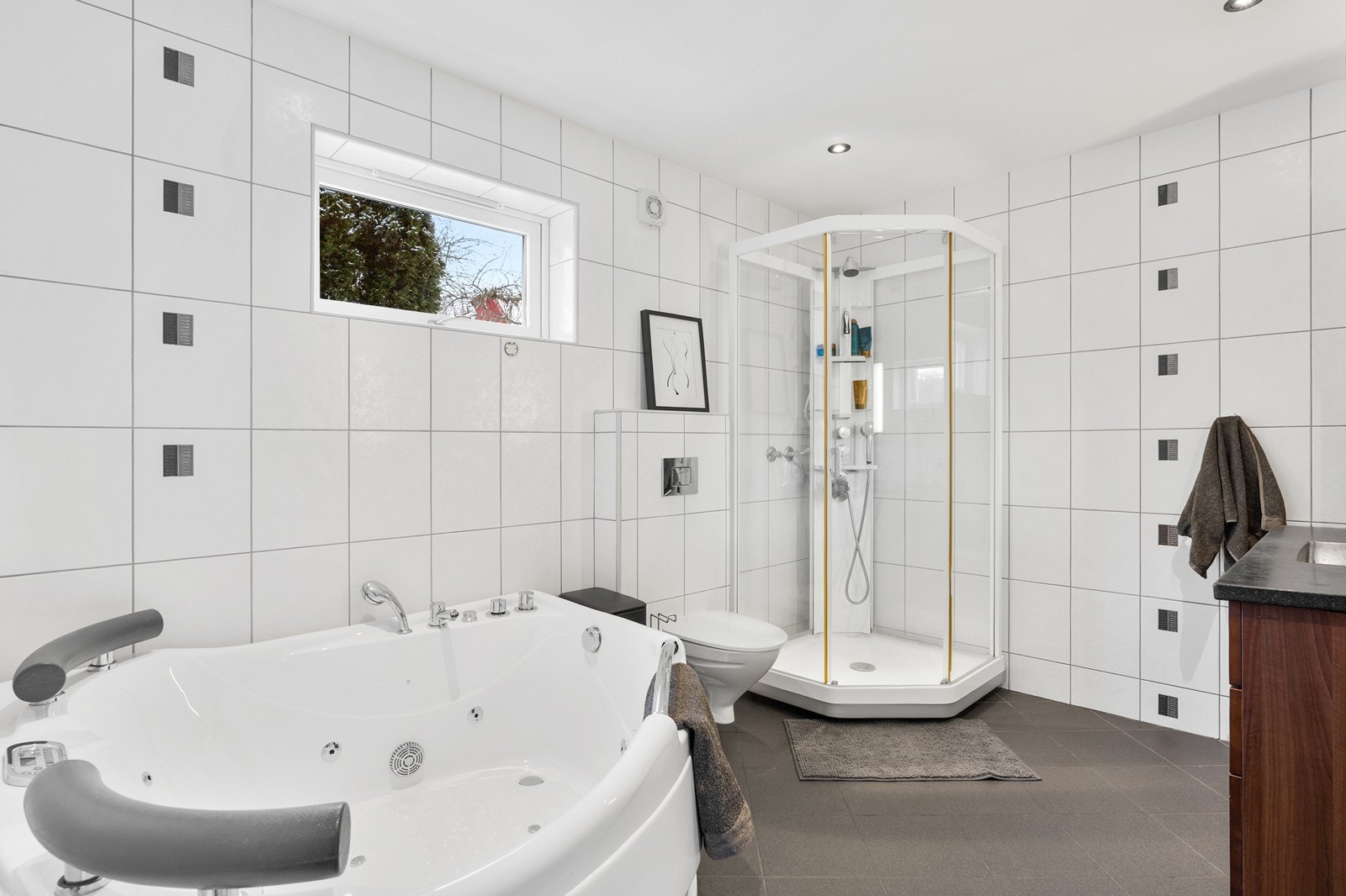 Badet er innredet med baderomsinnredning med nedfelt servant og sideskap, vegghengt toalett, dusjkabinett og badekar. Galleribilde