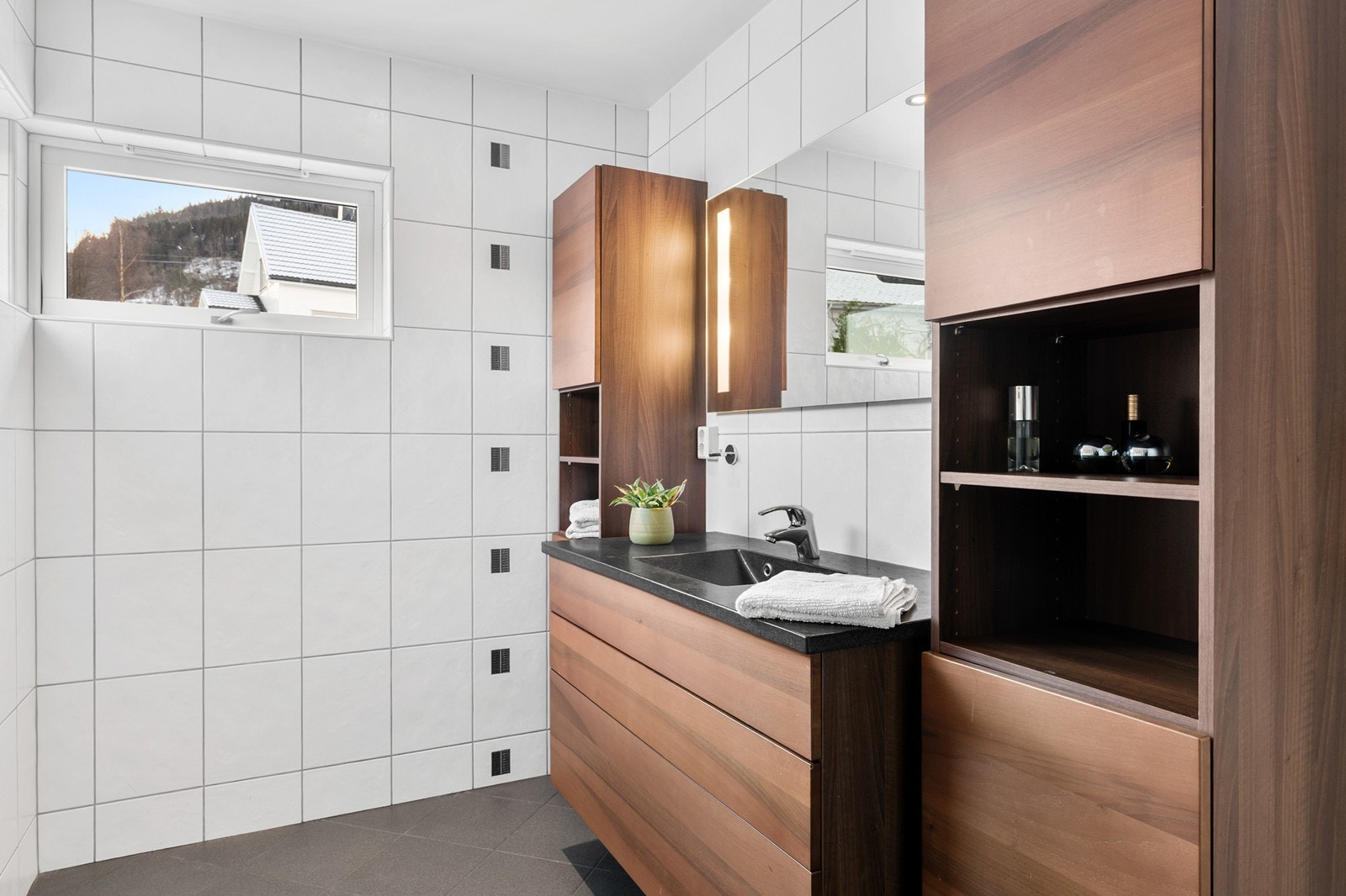 Badet er av god størrelse og inneholder servant med underskap samt sideskap på hver side, vegghengt toalett og dusjhjørne. Galleribilde