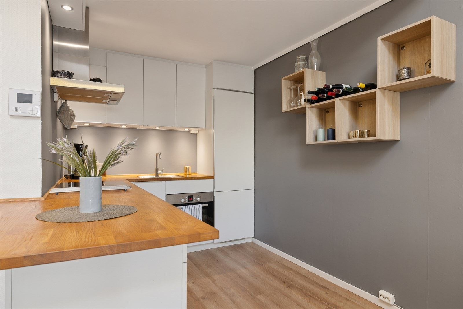 Pent kjøkken med innredningen som består av glatte fronter og benkeplater i laminert heltre. Det er integrerte hvitevarer som kjøl- og fryseskap, oppvaskmaskin, platetopp, stekeovn og vaskemaskin. Galleribilde