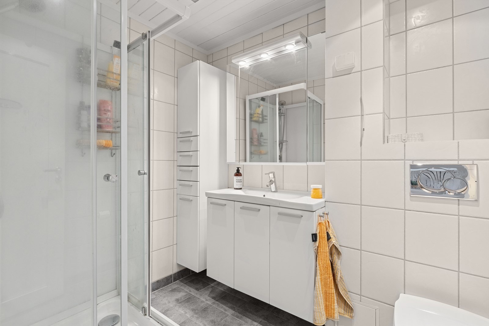 Badet har flislagte overflater og behagelig gulvvarme. Rommet er utstyrt med servantinnredning, høyskap, speilskap, toalett og dusjkabinett. Galleribilde