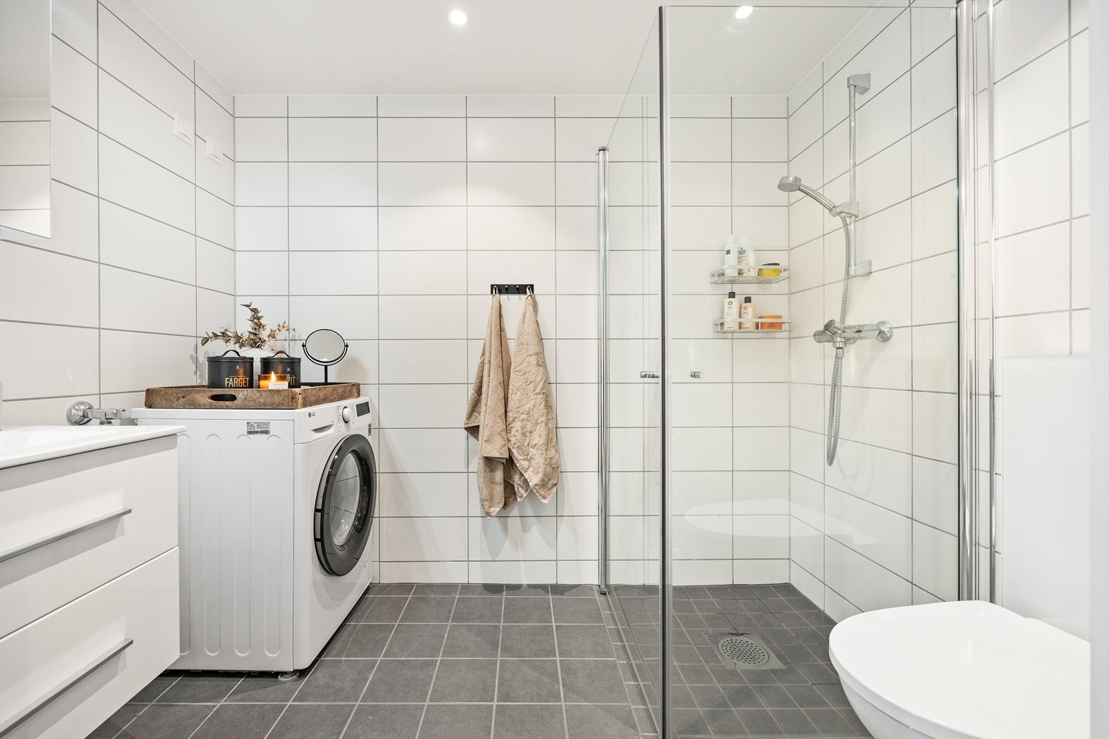 Pent flislagt bad med varmekabler i gulvet, utstyrt med dusjhjørne med innfellbare glassvegger, vegghengt toalett og servantinnredning med skuffer. Galleribilde