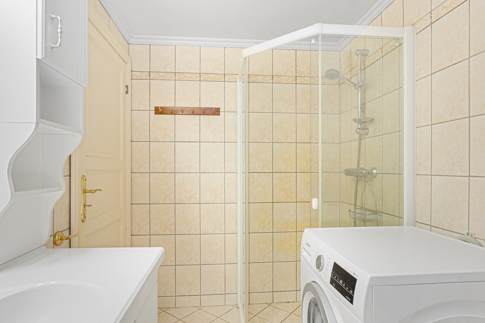 Rommet er innredet med hvit baderomsinnredning, gulvstående toalett, badekar, dusjhjørne og opplegg for vaskemaskin Galleribilde