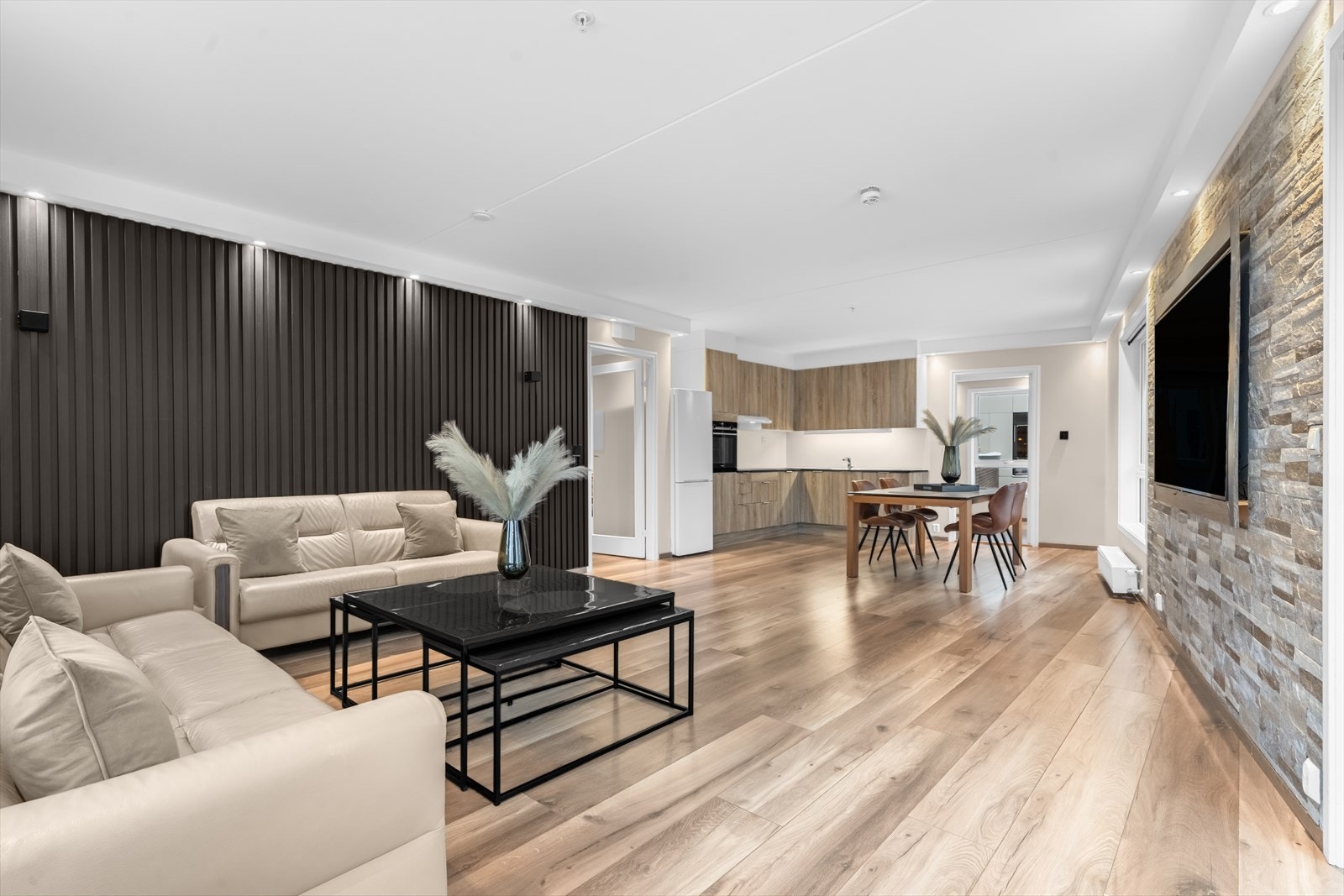 Åpen stue- og kjøkkenløsning med integrerte hvitevarer og nyere laminatgulv. Galleribilde