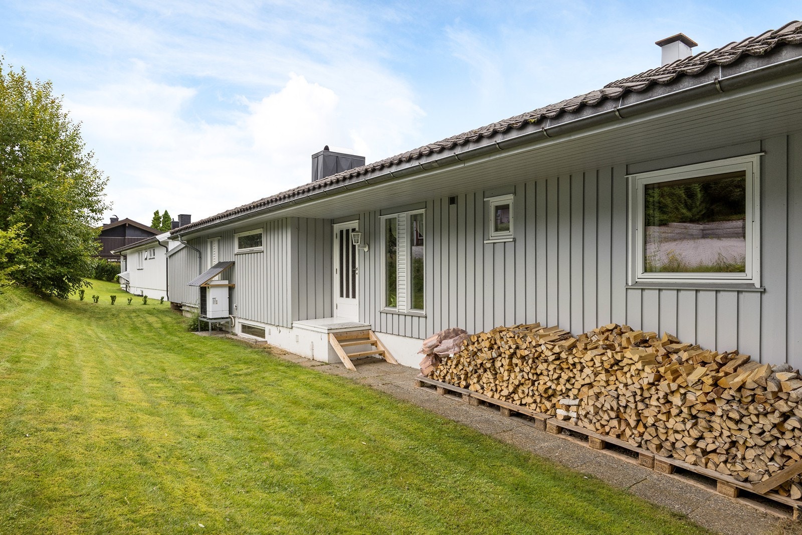 Bak boligen er det et lite plenområde og en hellelagt platting til adkomstterrasen som gir adgang til hovedetasjen. Galleribilde