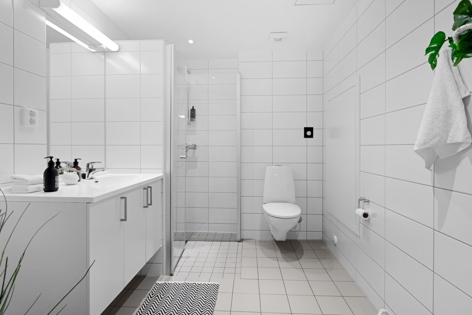 Pent flislagt baderom med varme i gulv. Badet er innredet med servantinnredning, toalett, dusjnisje med innfellbare glassdører og opplegg for vaskemaskin og tørketrommel i søyle. Galleribilde