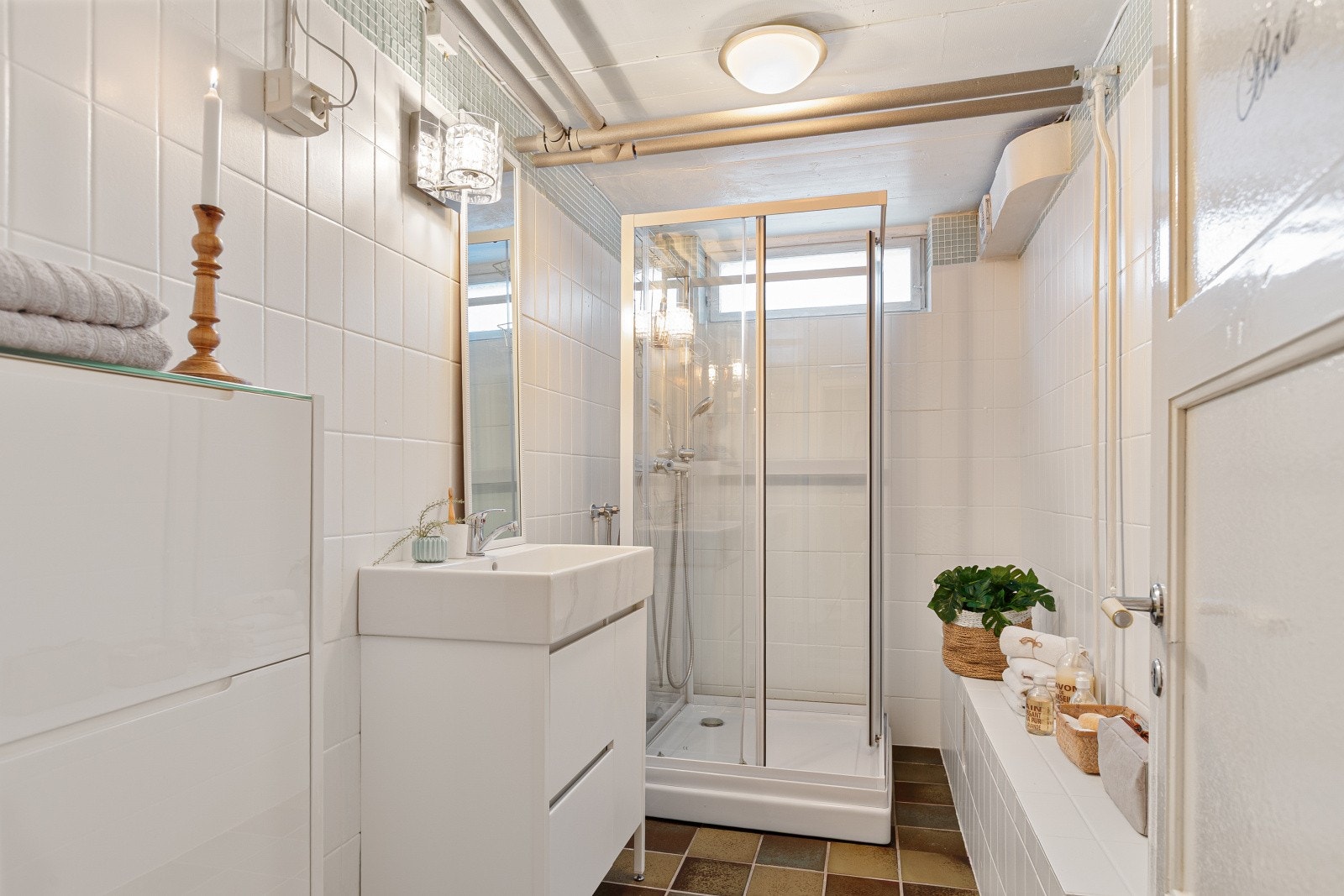 Badet i kjelleretasjen har fliser på gulv og vegg, enkel servant, helstøpt servant stående på innredning og dusjkabinett. Galleribilde