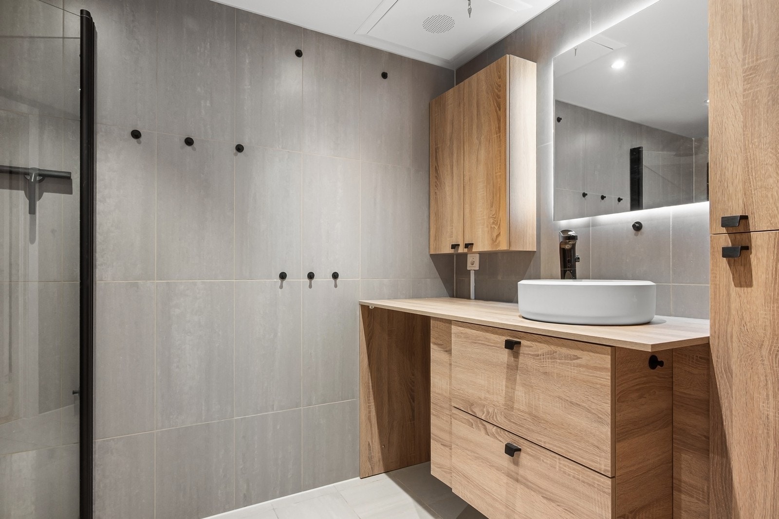 Innredningen består av dusjhjørne med glassvegger, veggfestet toalett samt stilren baderomsinnredning med skuffer og benkeplate. Over servanten er det speil med integrert belysning. Galleribilde