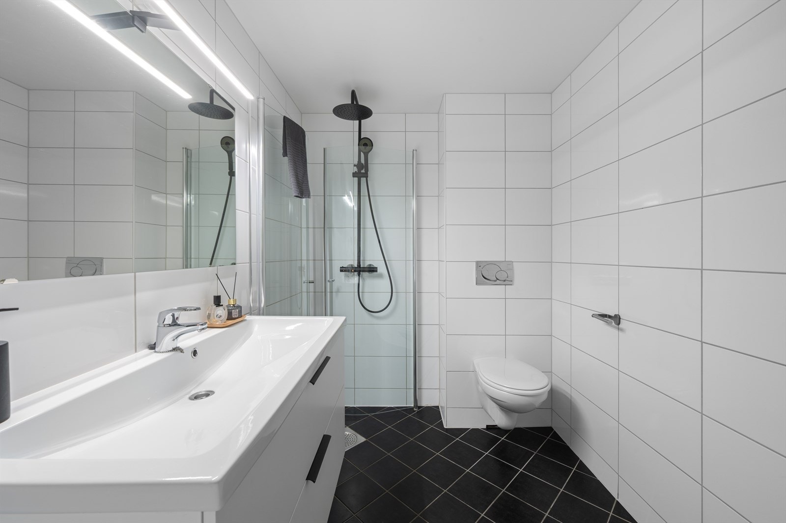 Baderommet er innredet med vegghengt servant i møbel, vegghengt toalett, praktisk dusjhjørne og opplegg til vaskemaskin. Galleribilde