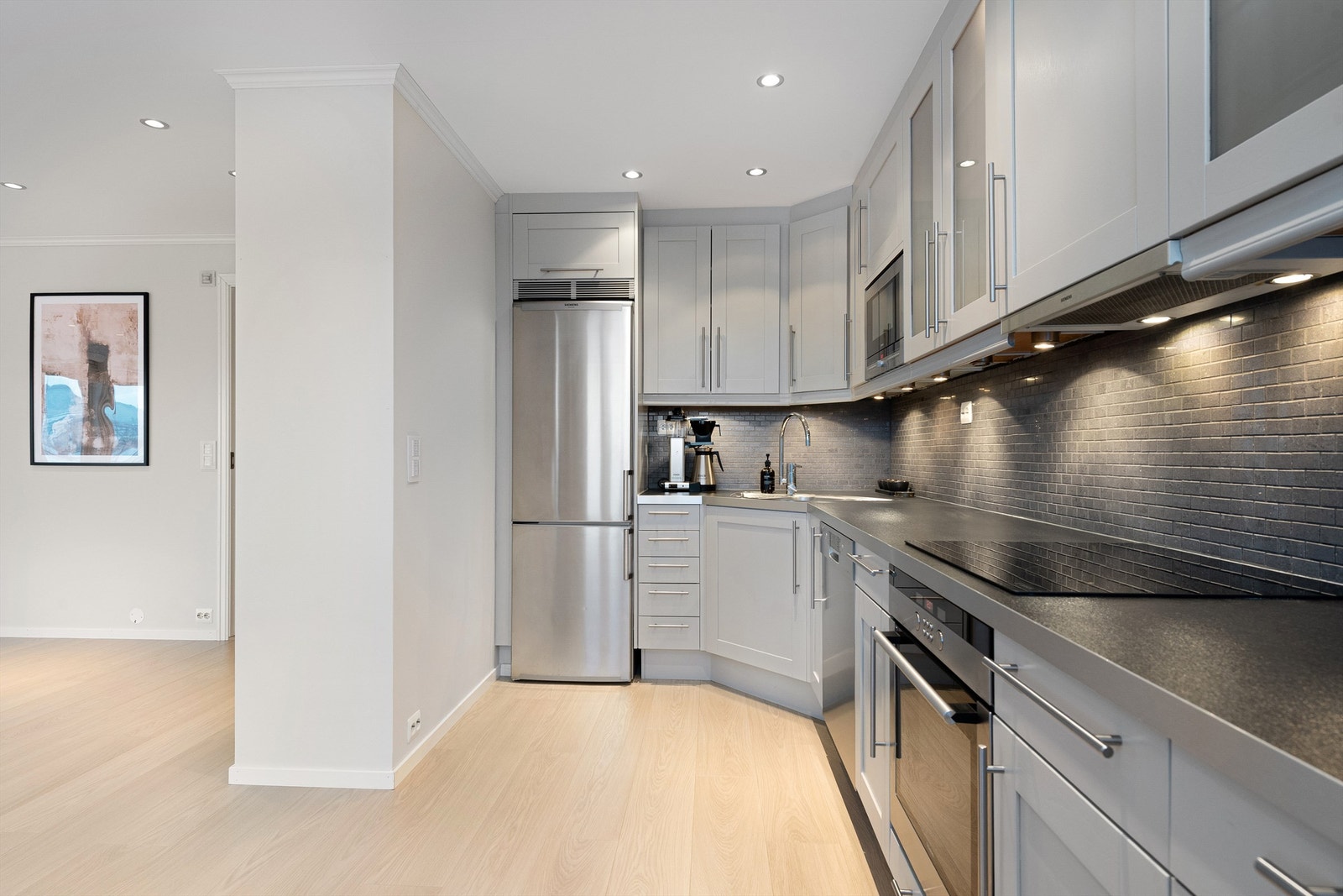 Integrert stekeovn og platetopp fra 2025. Frittstående oppvaskmaskin og kjøleskap med fryser. Ventilator i overskap. Det er lagt fliser mellom kjøkkenbenk og overskap. Galleribilde