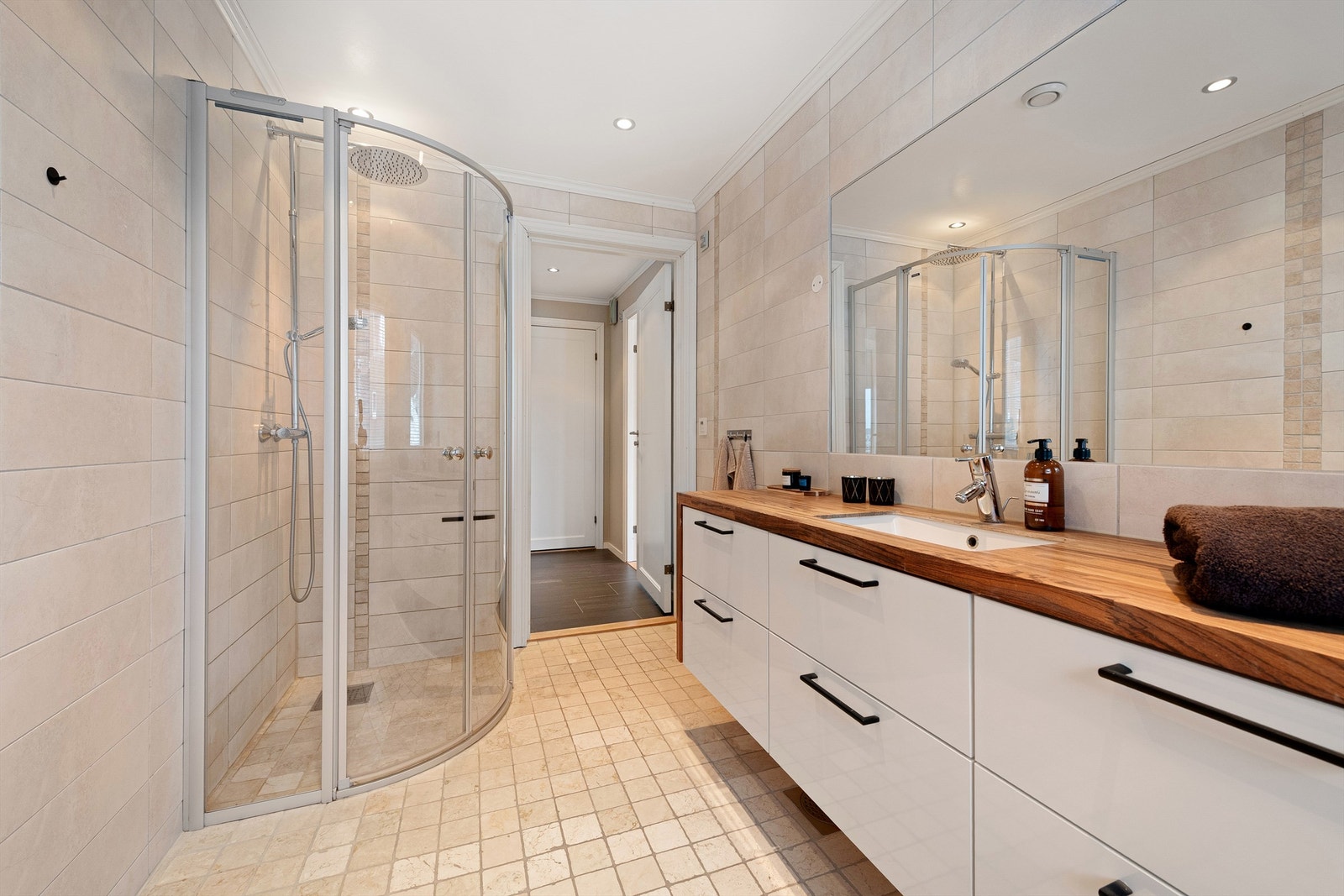 Flislagt bad med gulvvarme. Stor baderomsinnredning med skuffer og nedfelt servant med ett-greps armatur. Stort innfelt speil over servant. Dusjhjørne med dører og vegghengt dusjarmatur med hånddusj og regndusj). Vegghengt toalett. Galleribilde