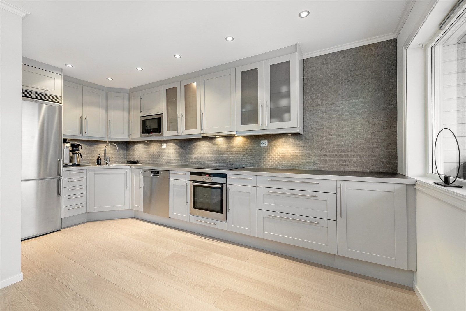 Kjøkkeninnredningen er fra Norema og har grå profilerte fronter og benkeplate av laminat med nedfelt oppvaskkum med ett-greps kjøkkenarmatur. Galleribilde