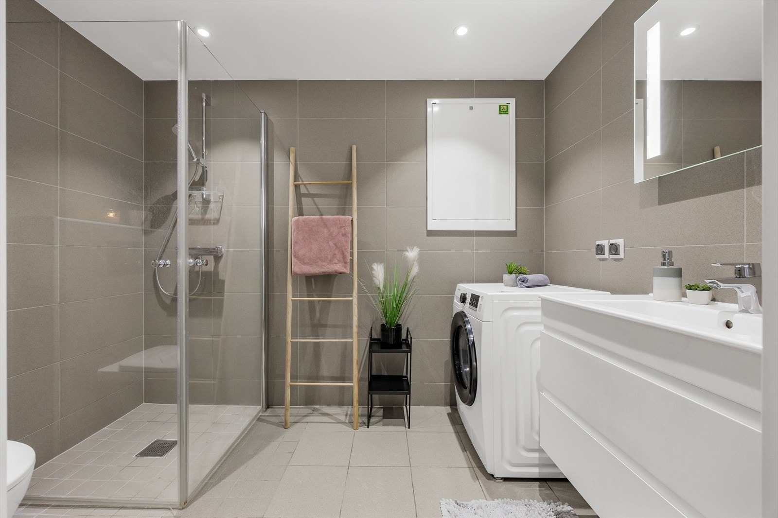 Helfliset bad med dusjhjørne, vegghengt toalett, baderomsinnredning med god lagringsplass og opplegg for vaskemaskin. Galleribilde