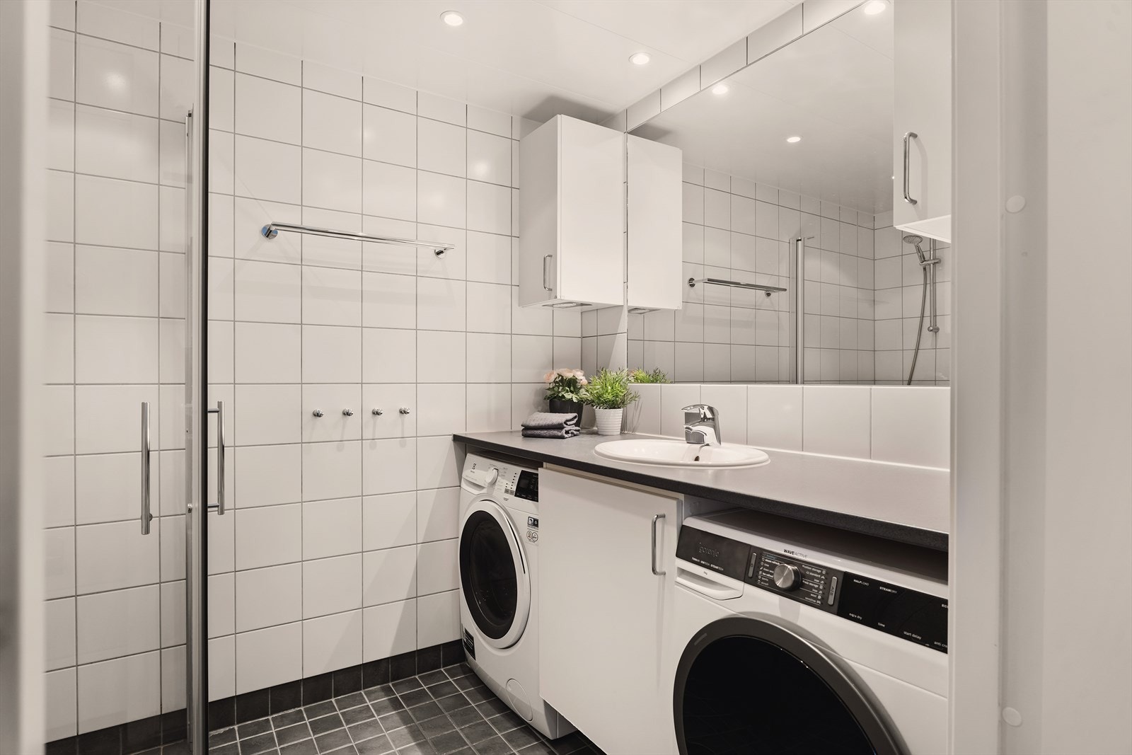 Flislagt bad med behagelig gulvvarme og himling med innfelte downlights med dimmer. Badet er utstyrt med vegghengt toalett, dusjhjørne, baderomsinnredning med under-/overskap og opplegg for vaskemaskin og tørketrommel. Galleribilde