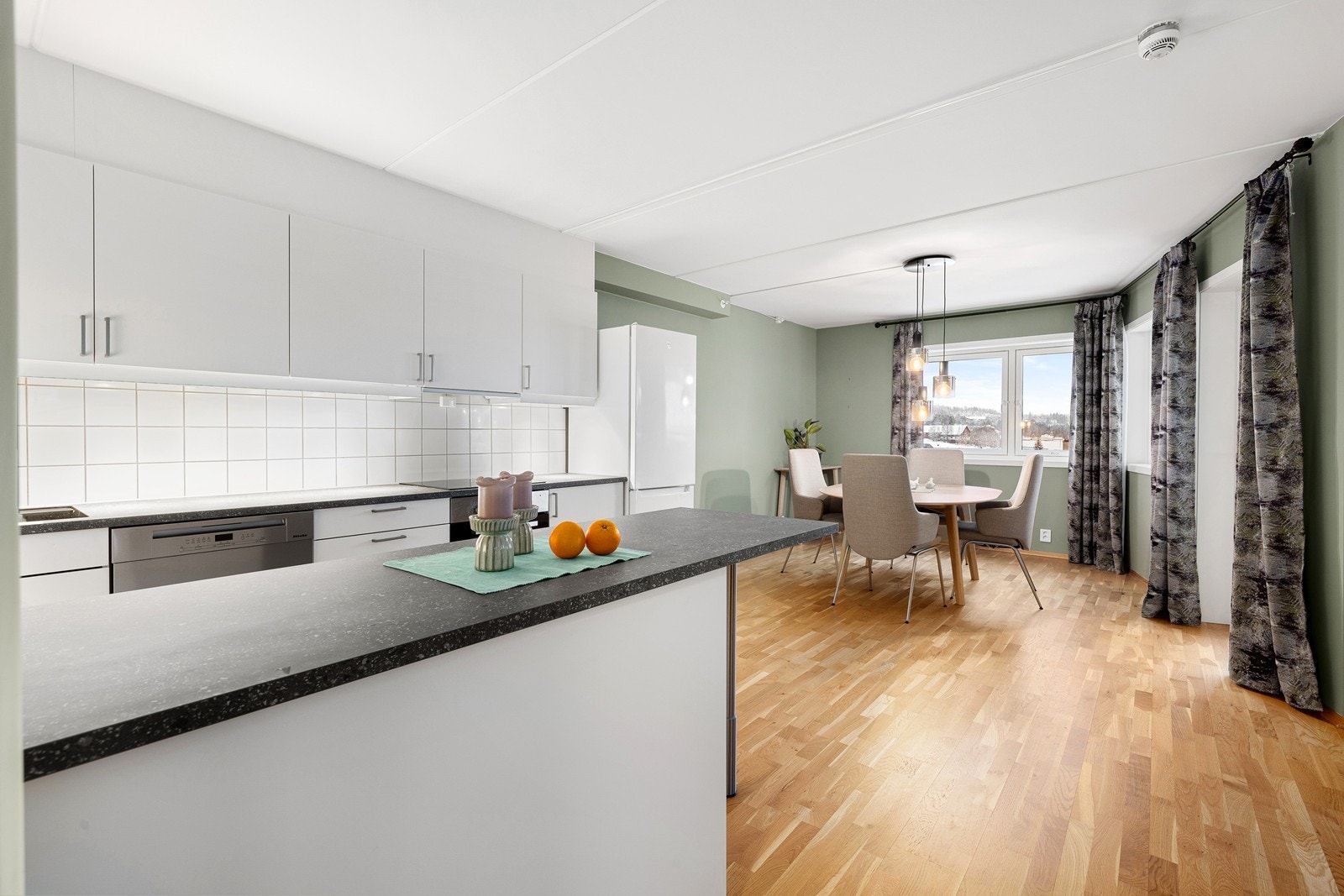 Videre kommer man inn i en åpen stue- og kjøkkenløsning malt i lyse farger. Galleribilde