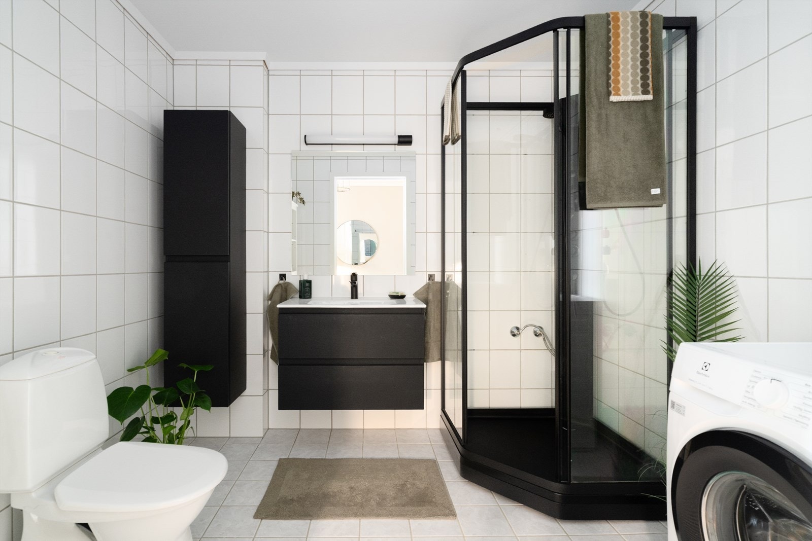 Pent og romslig baderom som er helfliset med varmekabler i gulvet. Her er det ny innredning og dusjkabinett fra 2025 i mørk utførelse. Badet har også toalett samt opplegg for og plass til vaskemaskin. Galleribilde