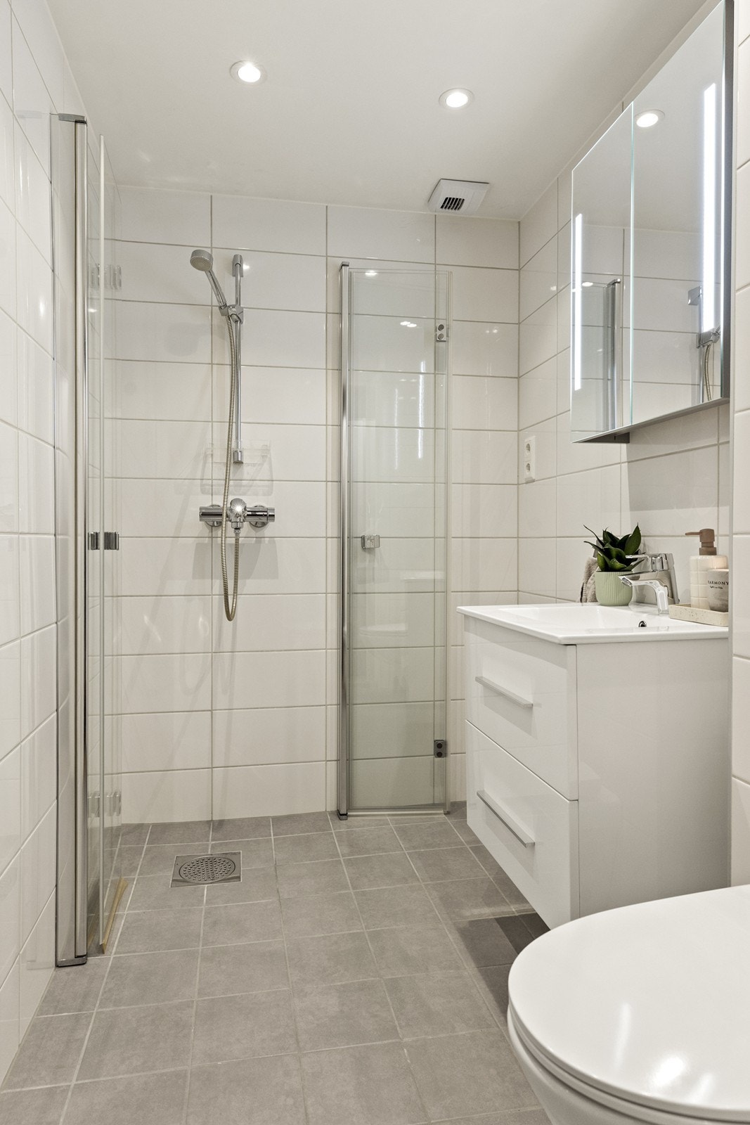 Helfliset bad med dusjhjørne med innfellbare glassdører og vegghengt toalett. Galleribilde