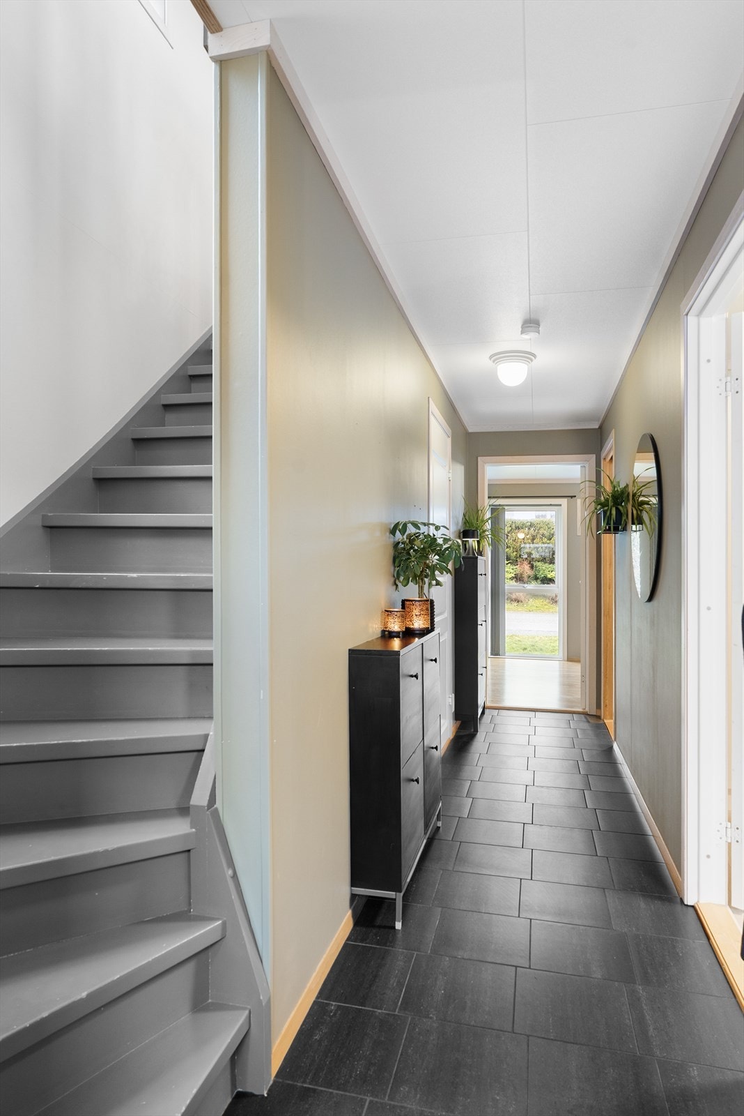 Romslig gang i 1. etasje med flislagt gulv med varmekabler - under trappen er det en praktisk bod/vaskerom med opplegg for vaskemaskin Galleribilde