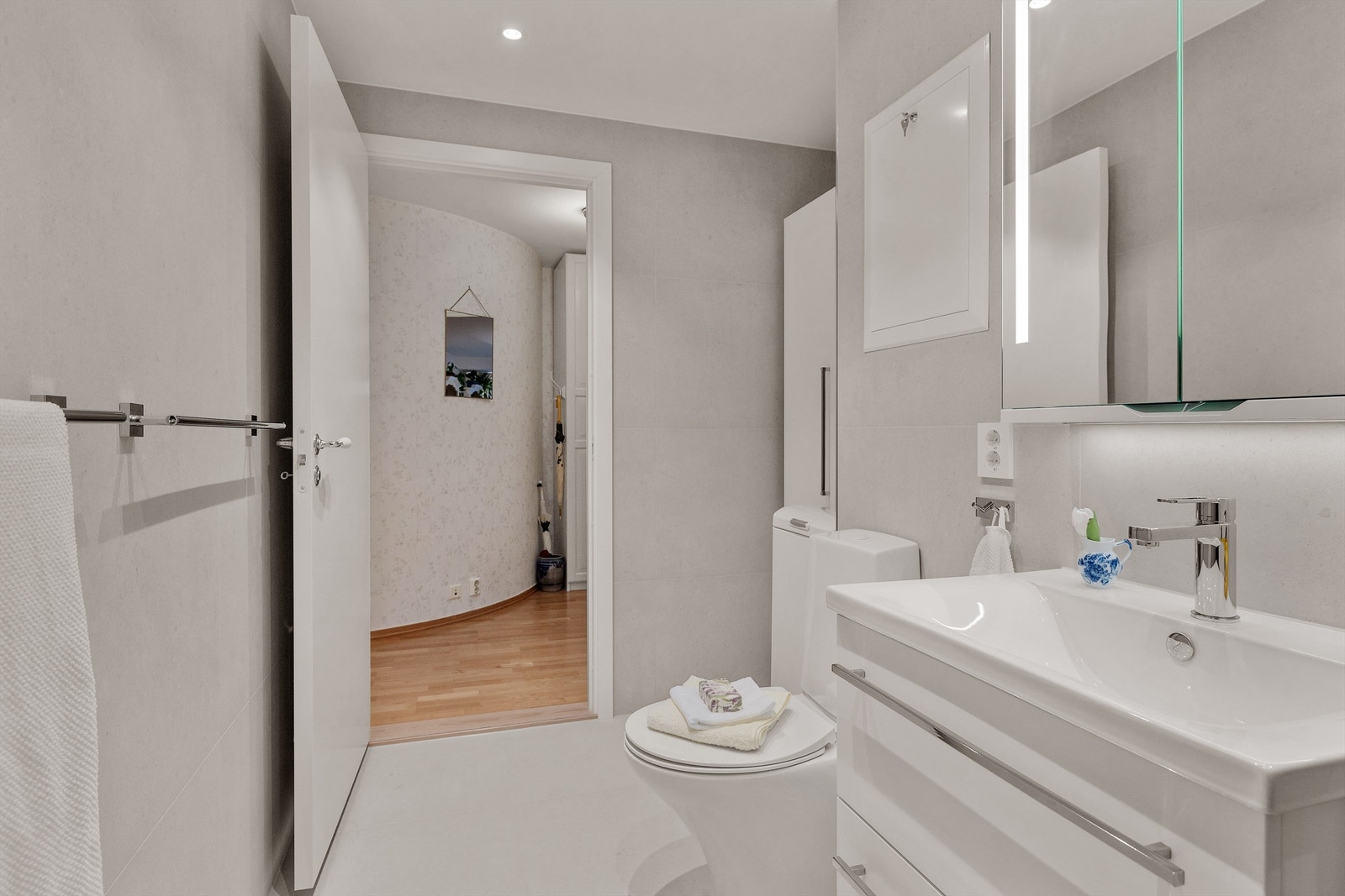 Badet består av vegghengt baderomsinnredning med glatte lyse fronter, heldekkende servant med ett-greps armatur og speilskap med belysning og stikkontakt over servant. Galleribilde