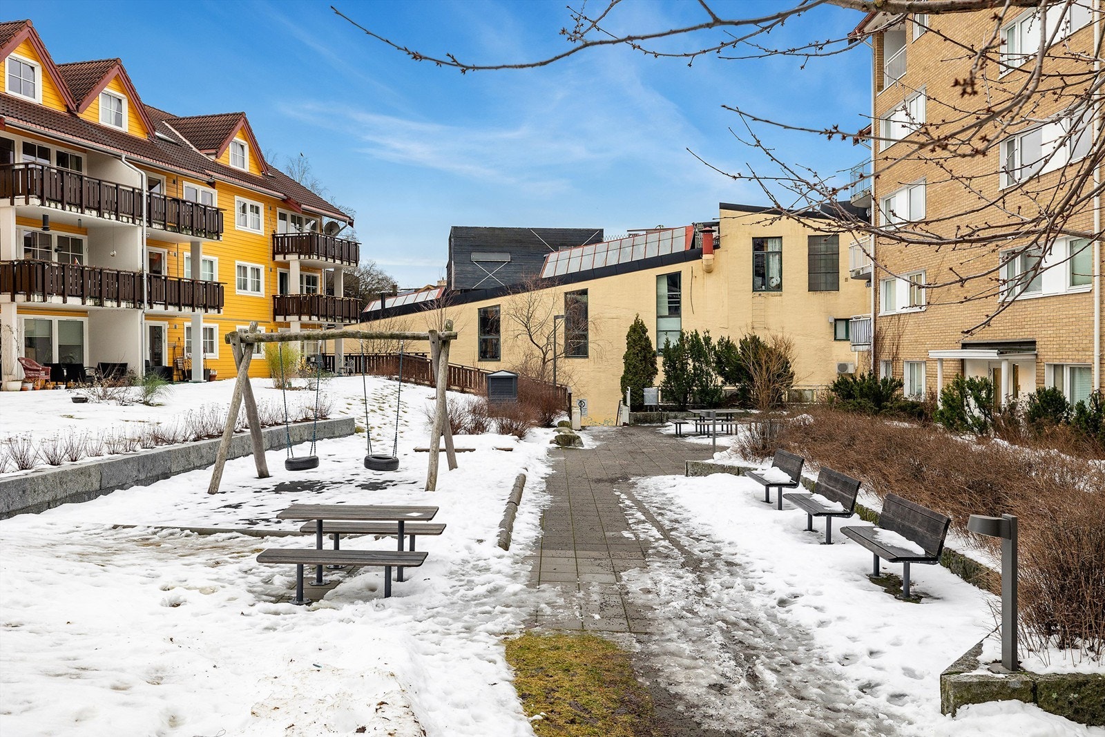 Koselige fellesområder på sameiets tomt, med sitteplasser, interne gangstier og lekestativer for de minste. Galleribilde