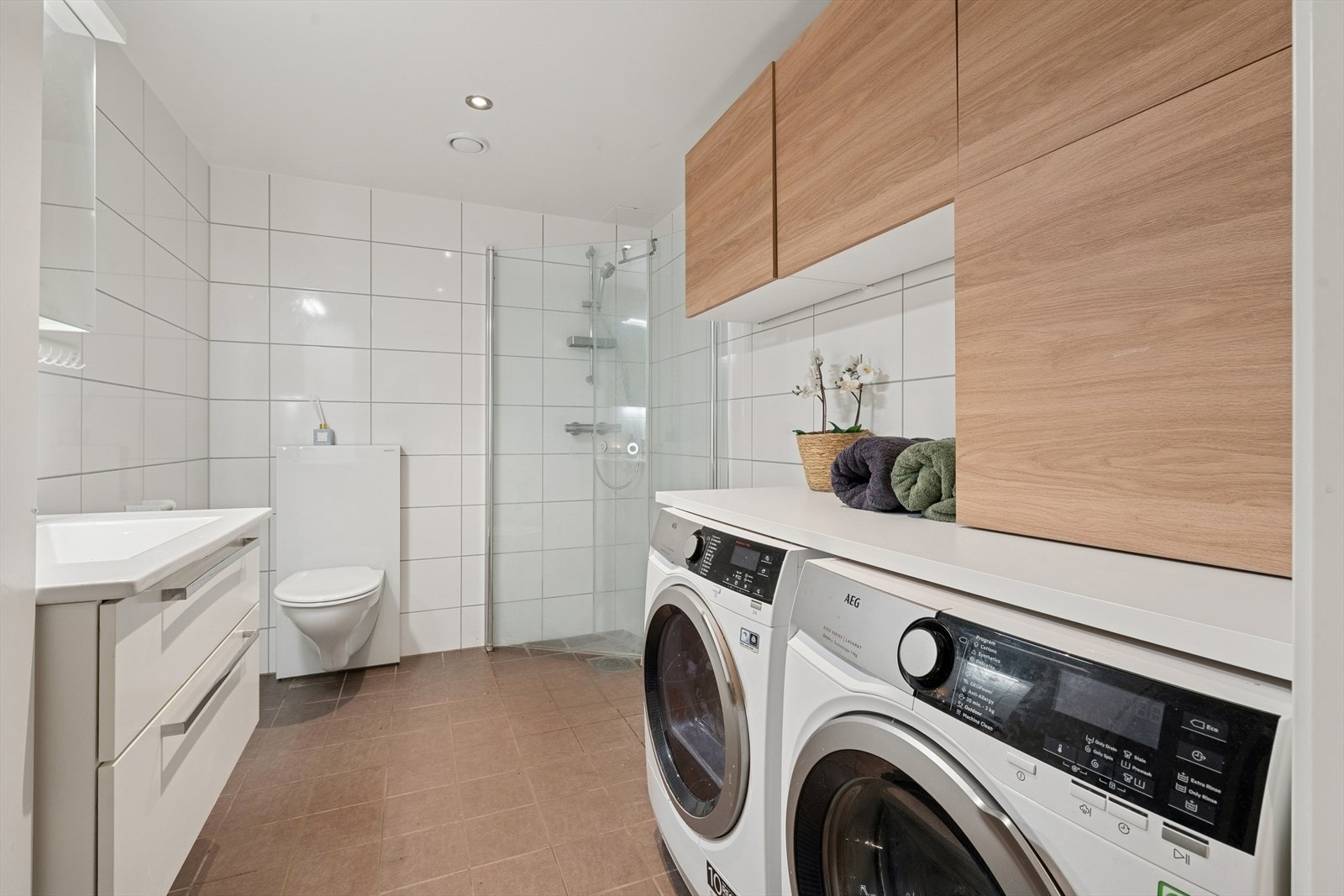 Moderne baderom med dusjhjørne og stilrene detaljer. Baderommet er av god størrelse med plassbygd benkeplass til vaskemaskin og tørketrommel. Det er også montert ekstra skap. Galleribilde