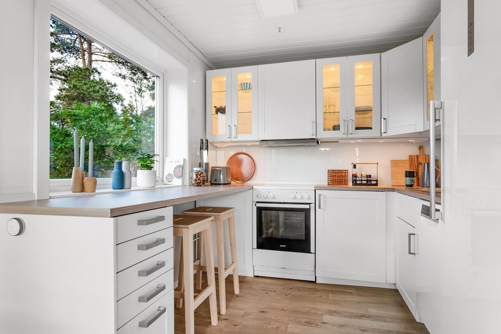 Pent kjøkken med vinduspost og spiseplass ved kjøkkenbenken. Ikea kjøkkeninnredning fra 2014 med profilerte fronter og laminert benkeplate. Galleribilde