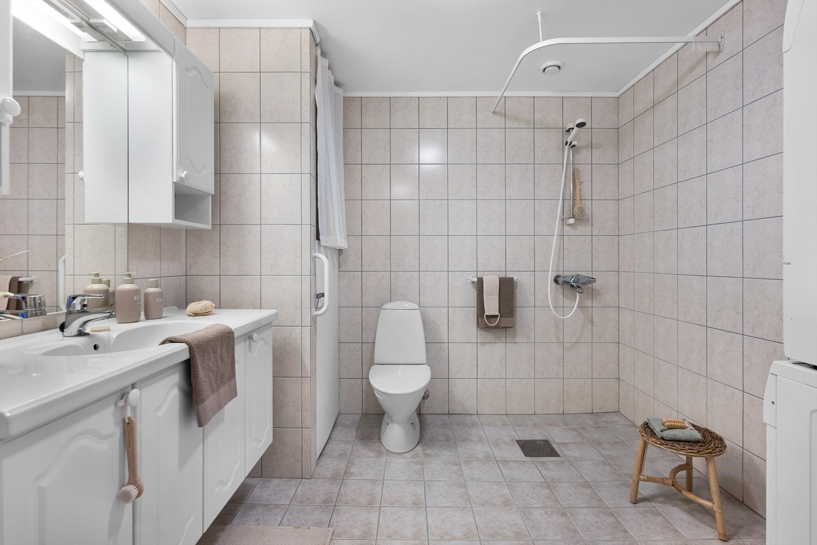 Helfliset bad innredet med toalett, dusjhjørne, opplegg for vaskemaskin og skapinnredning med servant Galleribilde