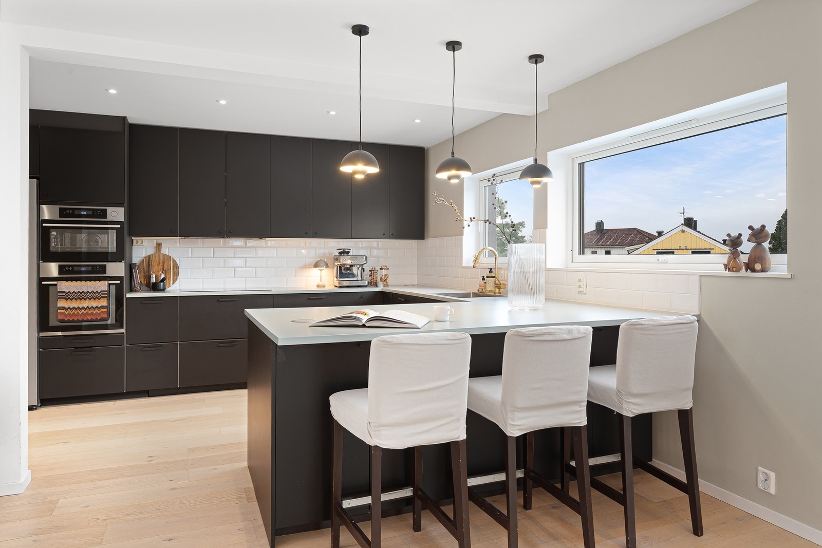 Detalj fra kjøkkenet med moderne innredning, integrerte hvitevarer og hyggelig barløsning mot vindu som gir godt naturlig lys. Galleribilde