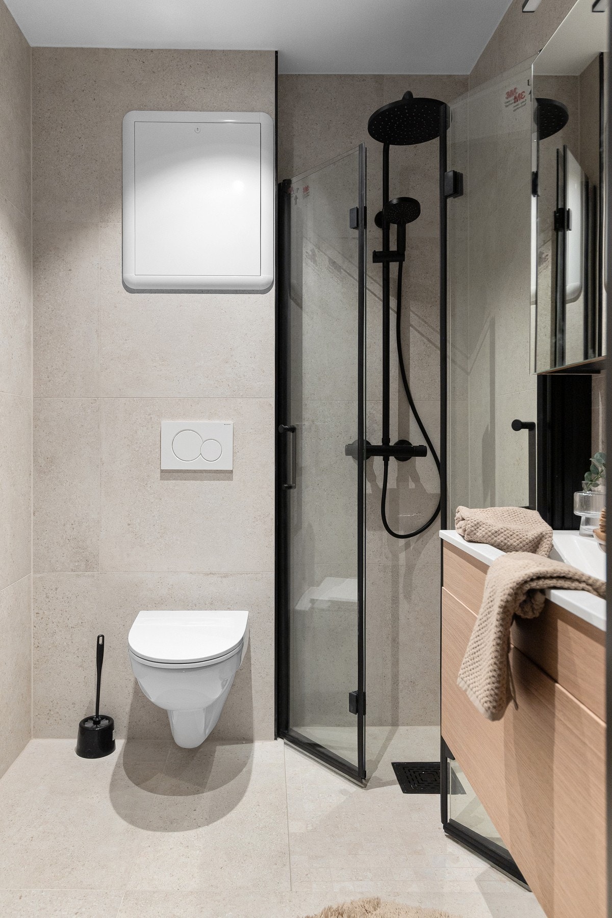 Innredet med vegghengt toalett, servant med innredning, speilskap og dusjhjørne med dusjdører i glass som er sammeleggbare. Galleribilde