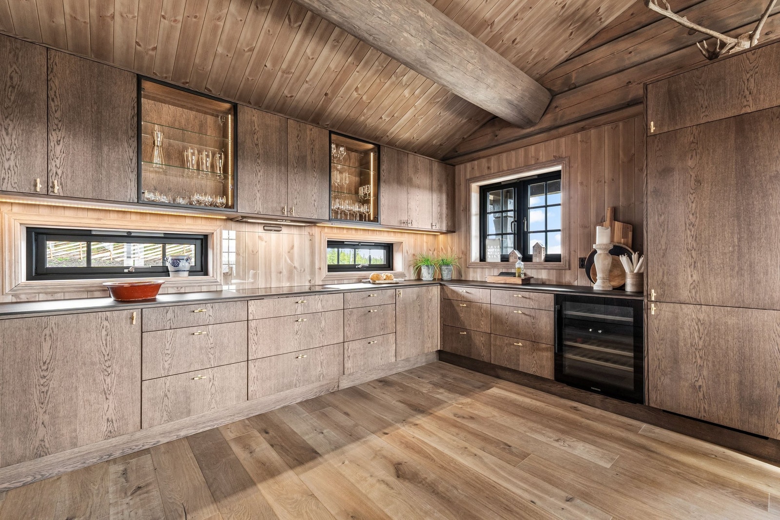 Fronter på kjøkkeninnredning med eike-finerte fronter, høytrykkslaminat benkeplate med nedsenket koketopp og underlimt oppvaskkum. Romslig 2-soners vinskap Galleribilde