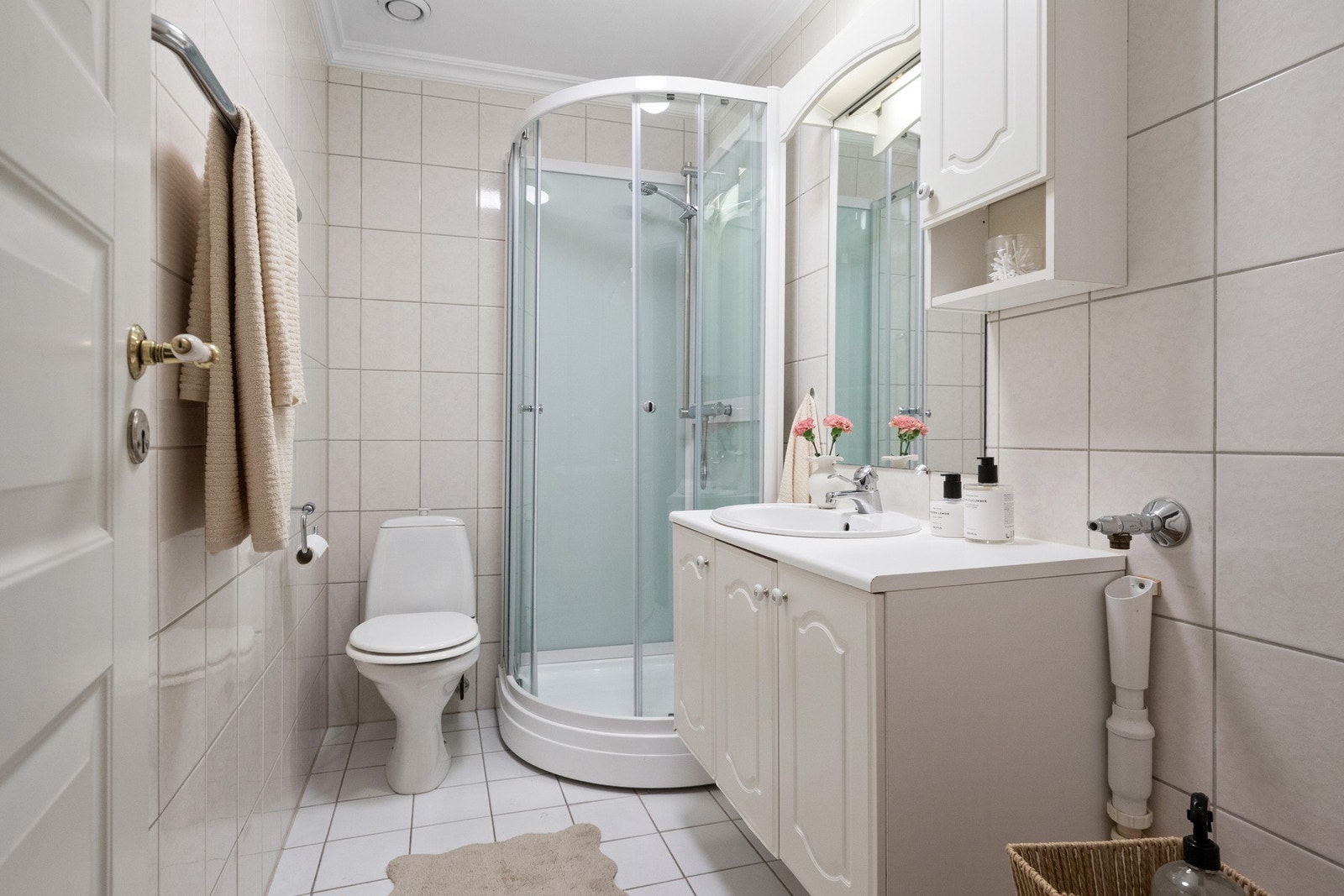 Badet har hvite gulvfliser og beige veggfliser. Det er varmekabler i gulv og opplegg for vaskemaskin. Galleribilde