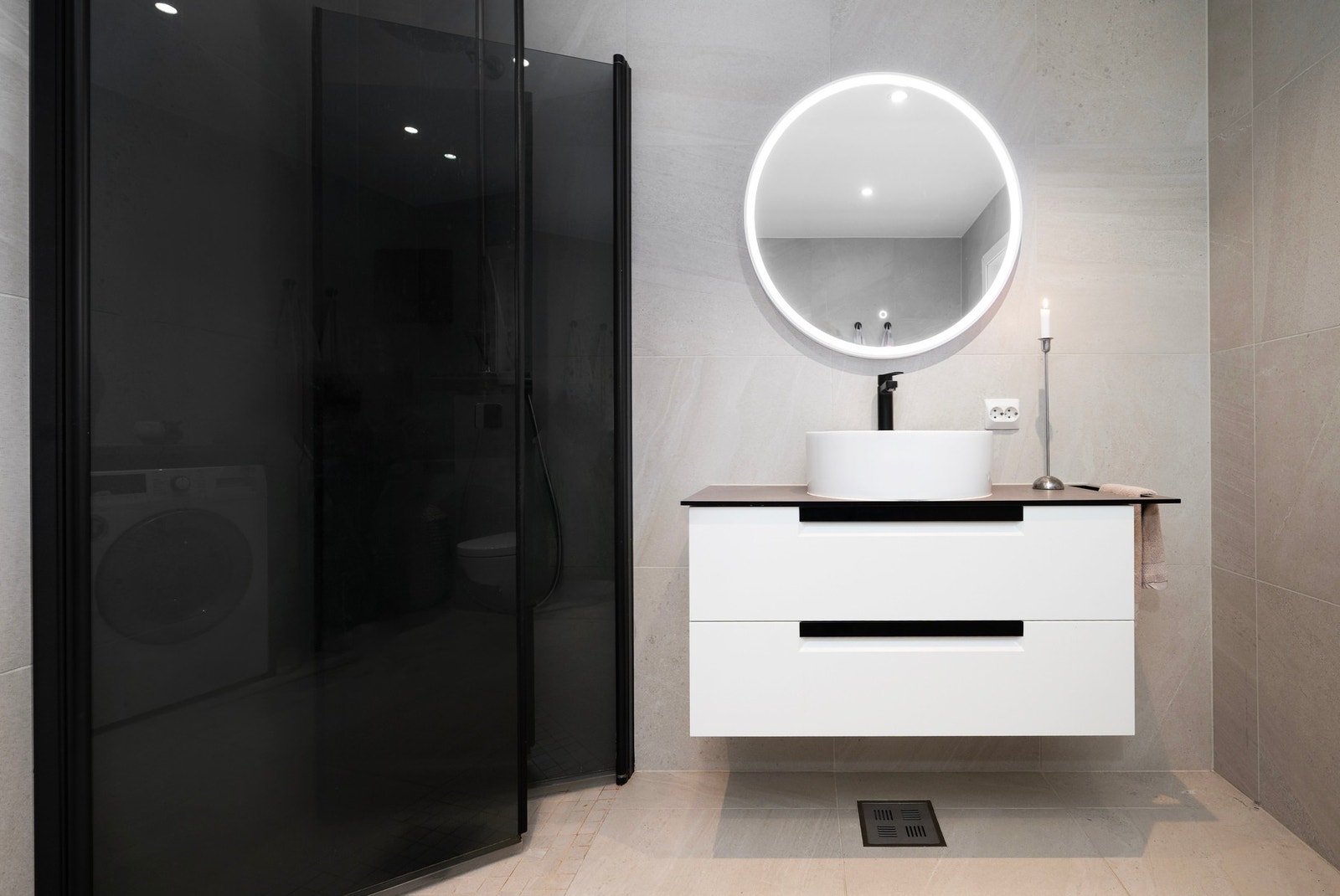 Smakfullt baderom med sotete dusjdører, rund servant og speil med lys. Galleribilde