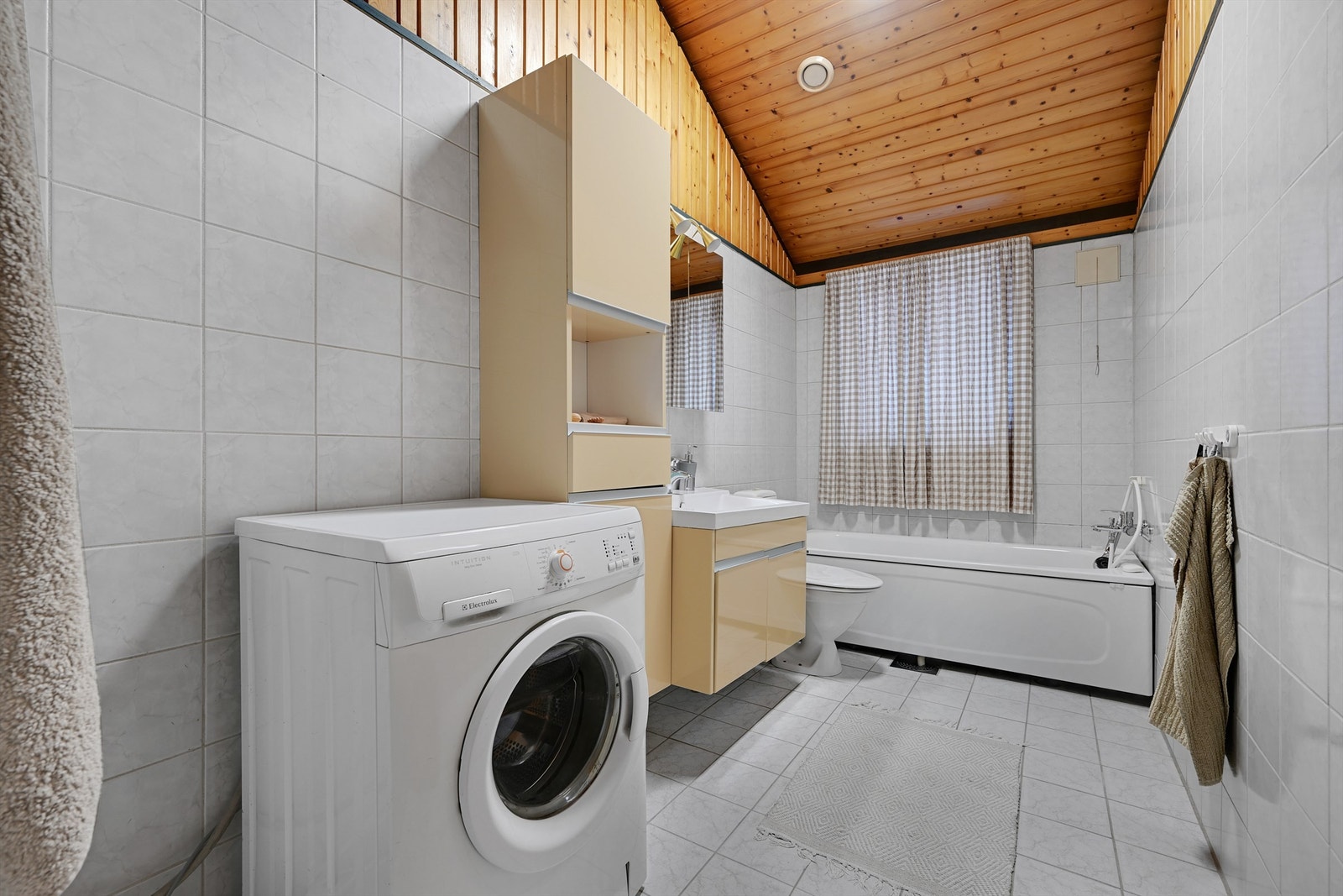 Badet i hovedetasjen er flislagt på gulv og vegger, med varmekabler i gulvet. Her finner du badekar, servant i baderomsinnredning og opplegg for vaskemaskin. Galleribilde