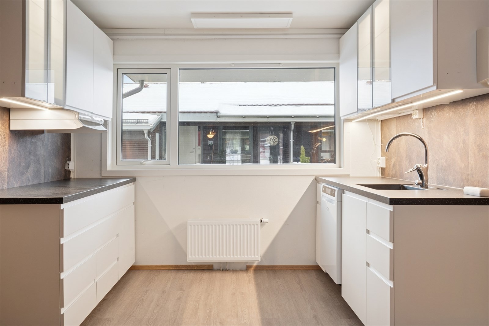 Fra gangen kommer man inn til kjøkken og spisestue som ligger i åpen løsning. Kjøkkenet er byttet i senere tid og tidløst innredet med hvite, slette fronter og mørk benkeplate i laminat. Galleribilde